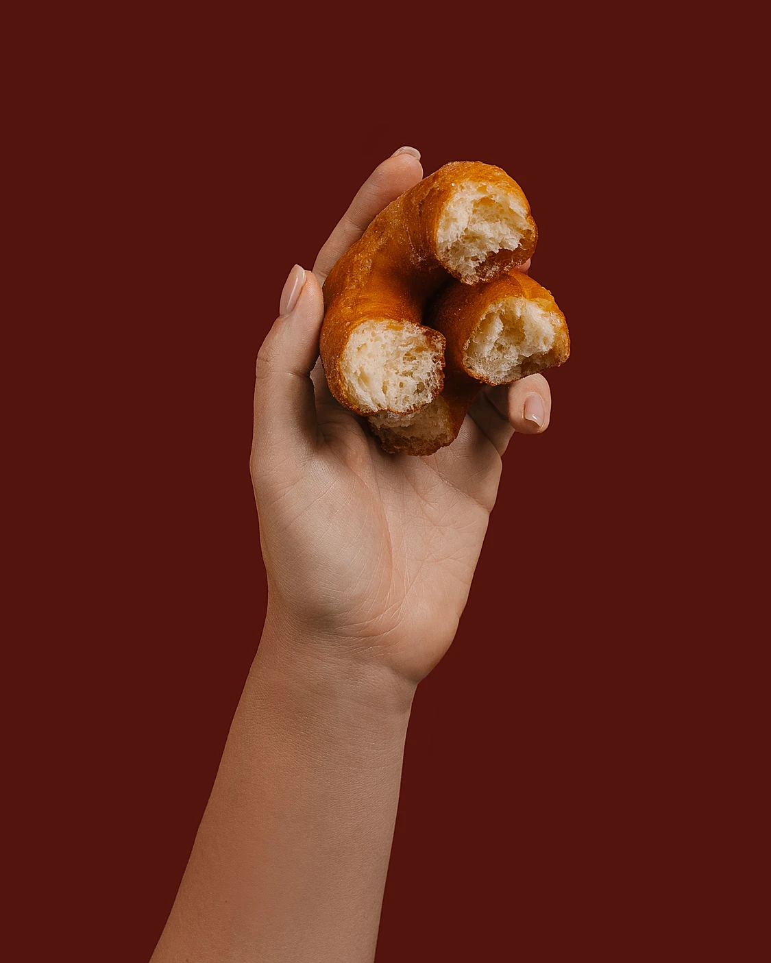 Hand holding a freshly fried homemade donut, golden-brown and broken to show its light, fluffy interior.