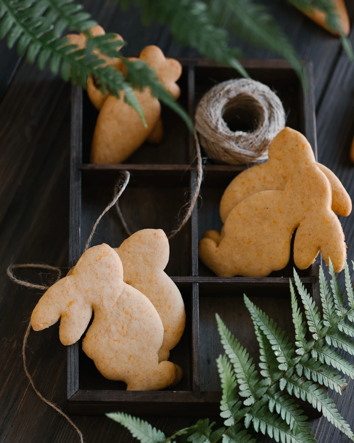Pumpkin cookies shaped like bunnies and carrots, arranged in a wooden box with twine and fern.
