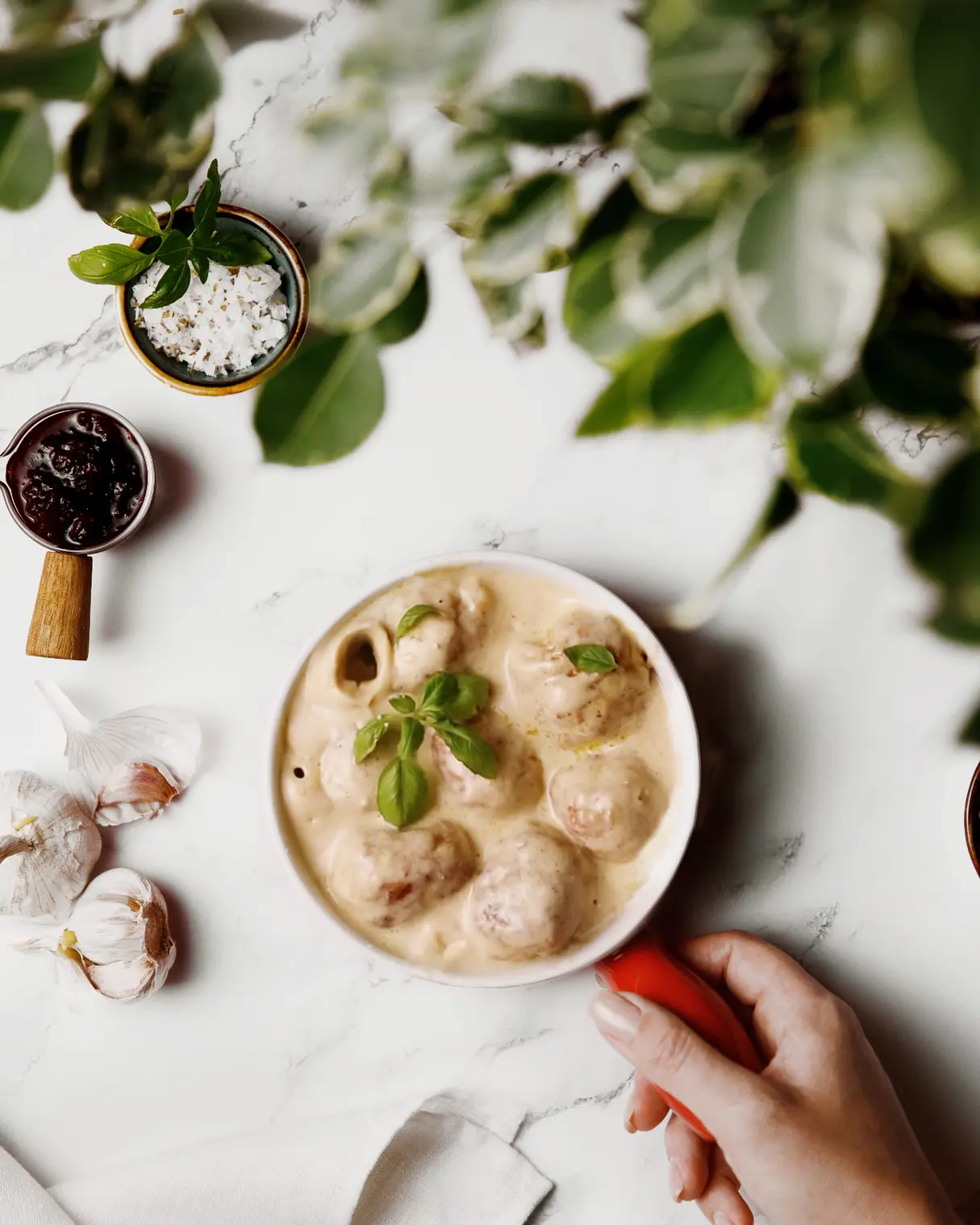Meatballs in rich creamy sauce with fresh basil garnish, garlic cloves nearby for this delicious recipe.