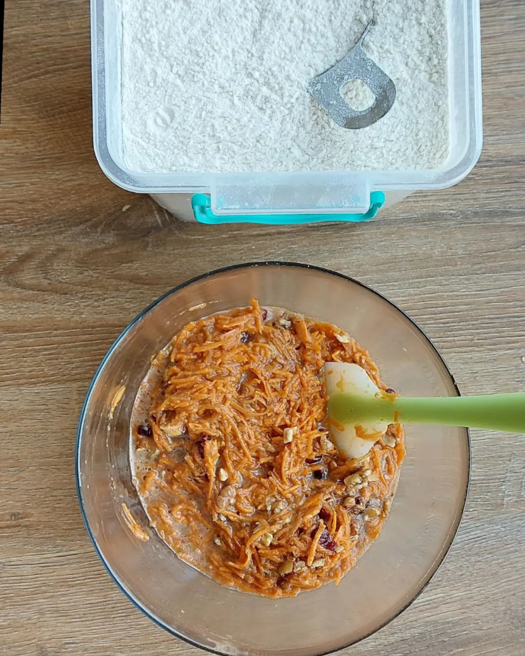 Mixing fresh carrots, walnuts, & cranberries in a bowl for the carrot cake recipe. Flour container nearby.