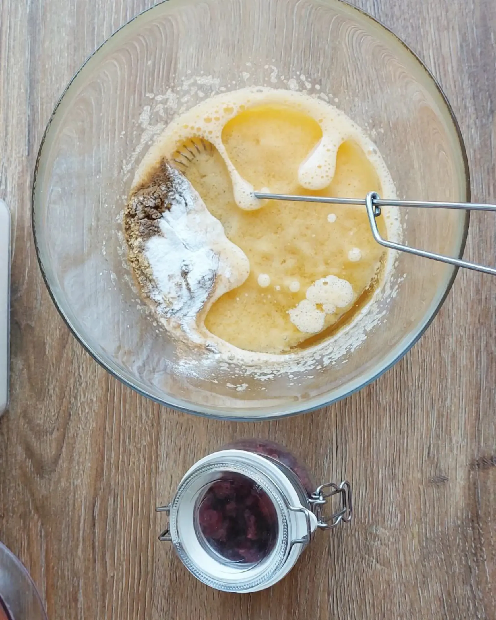 Carrot cake batter mixing: wet ingredients with flour, spices, baking powder. Jar of dried cranberries nearby.
