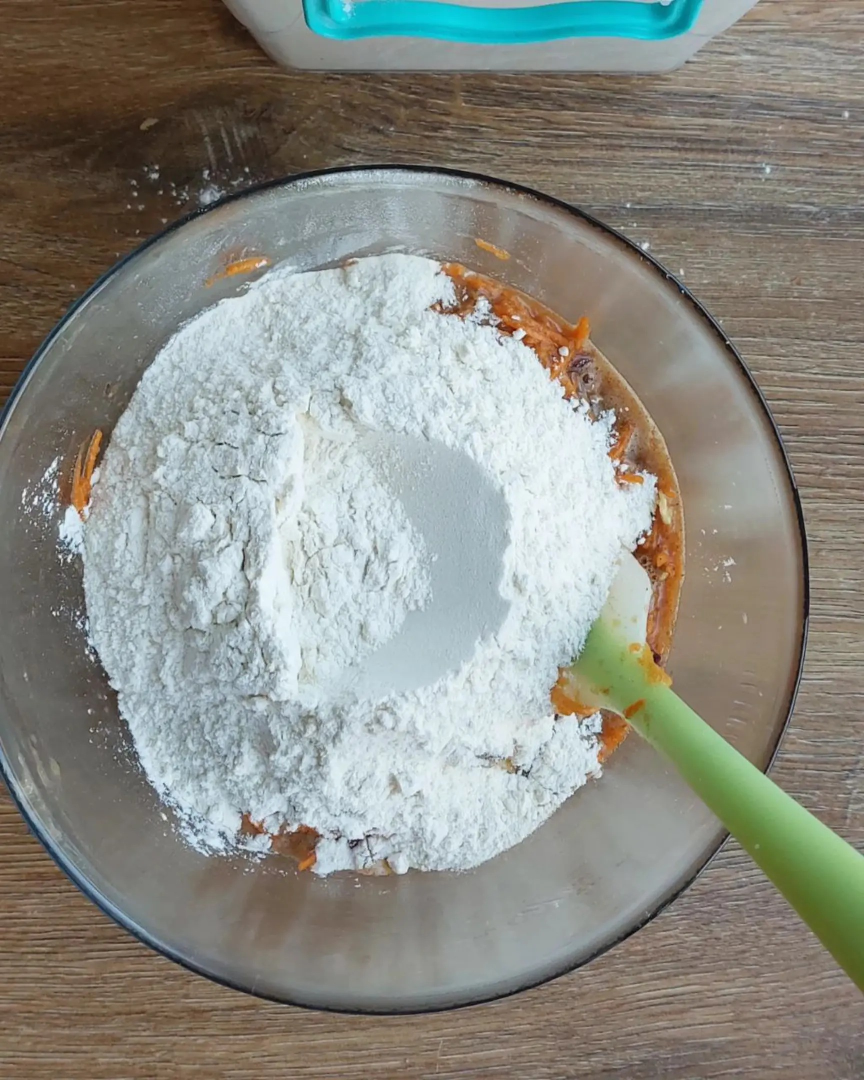 Flour and dry ingredients added to moist carrot cake batter in a glass bowl, preparing the delicious cake recipe.