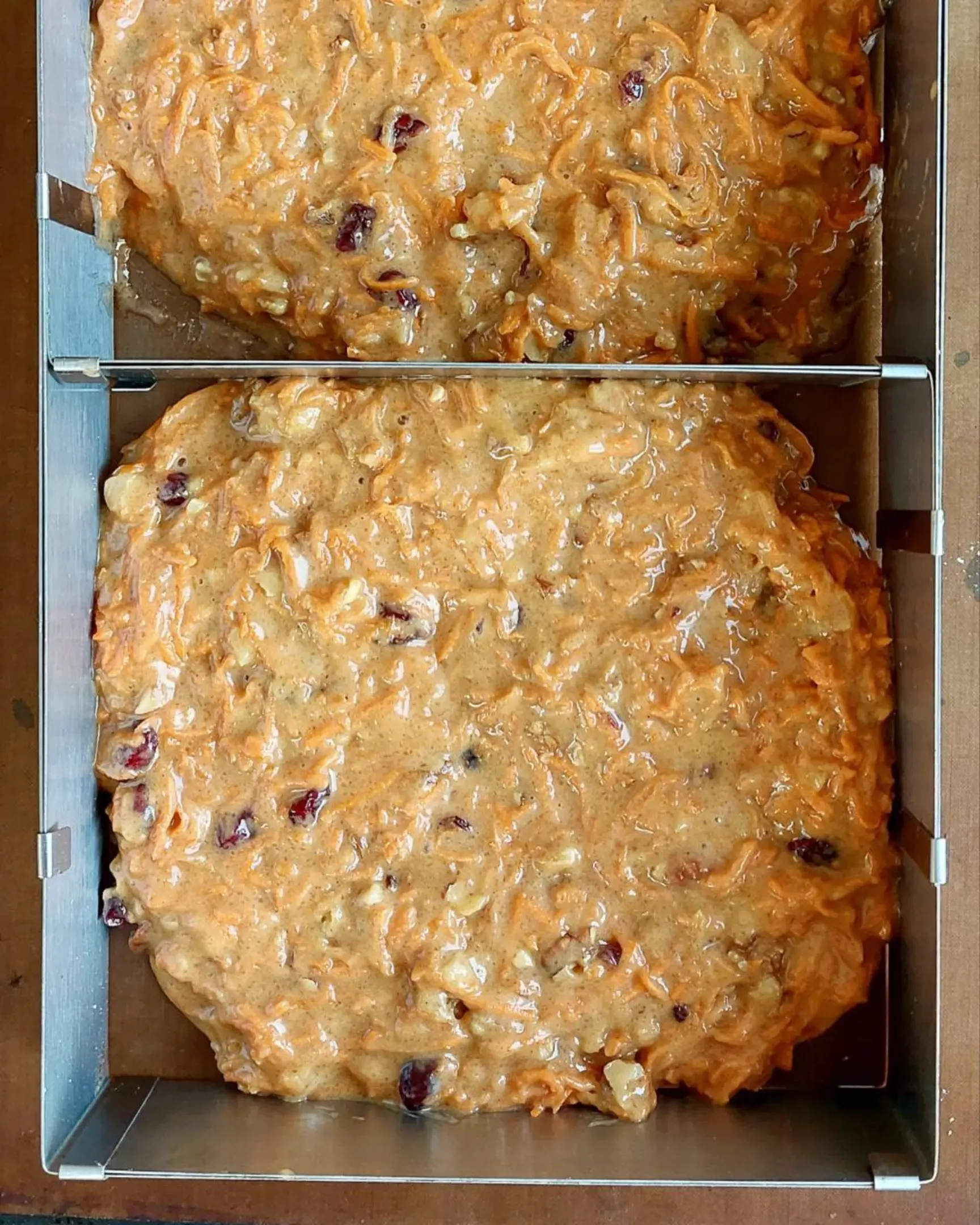 Moist carrot cake batter with fresh carrots, walnuts, and dried cranberries in metal baking molds, ready for baking.