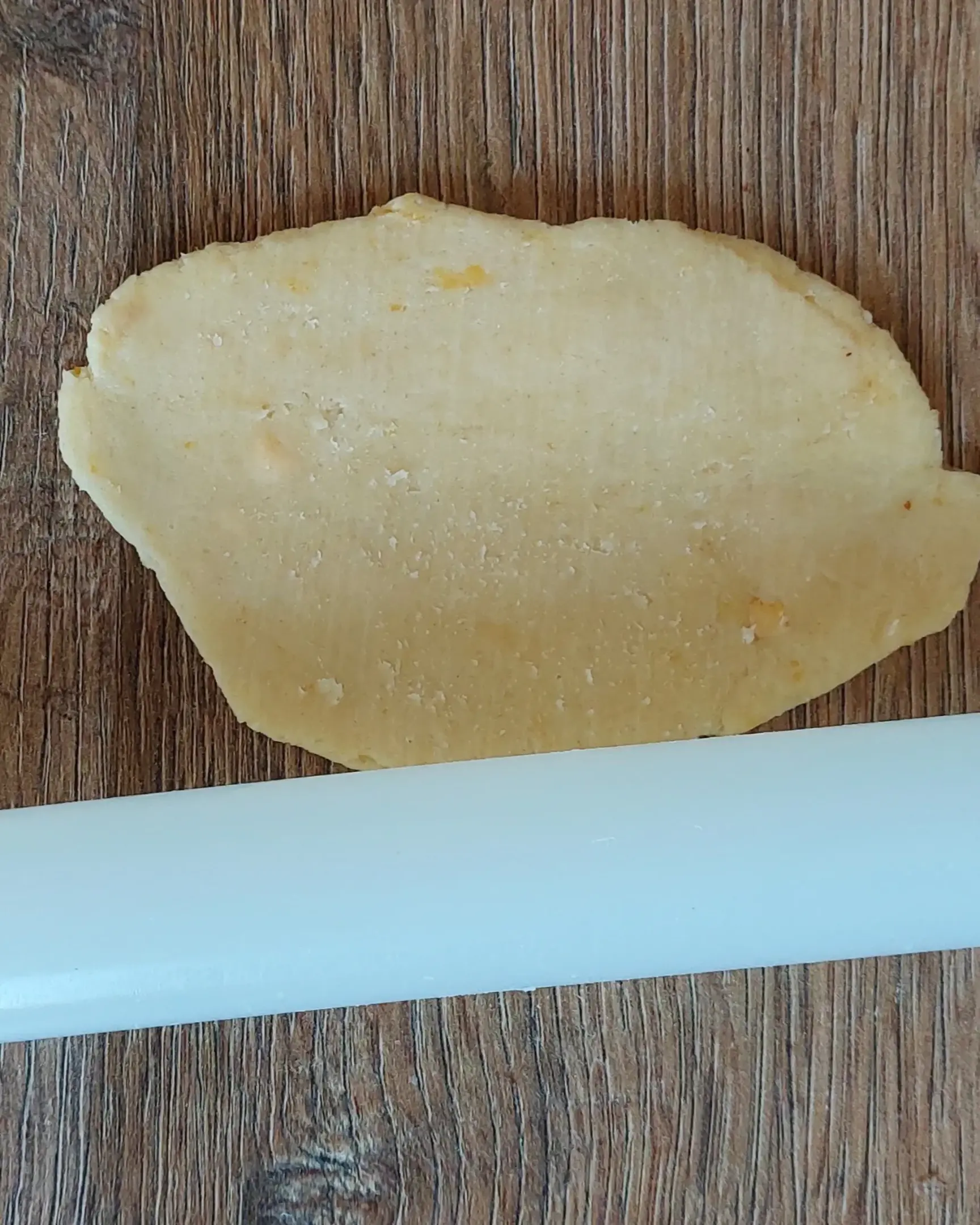 Овално тесто за маслени бисквитки, разточено на дървен плот с бяла точилка за печене.