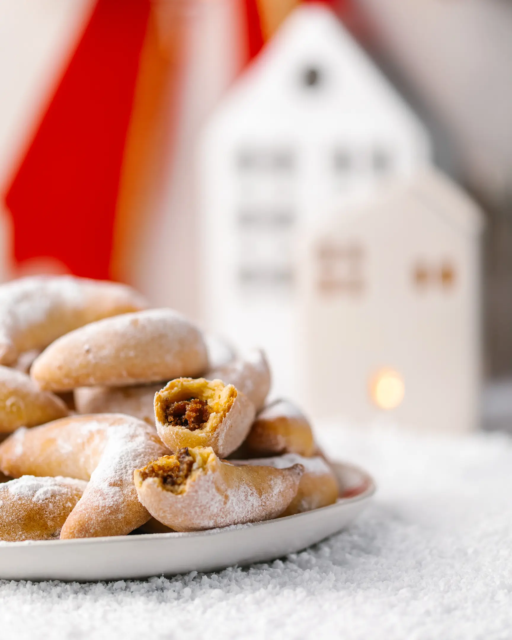 Нежни маслени сладки полумесеци с плодов и ядков пълнеж, поръсени с пудра захар, на чиния със зимен декор.