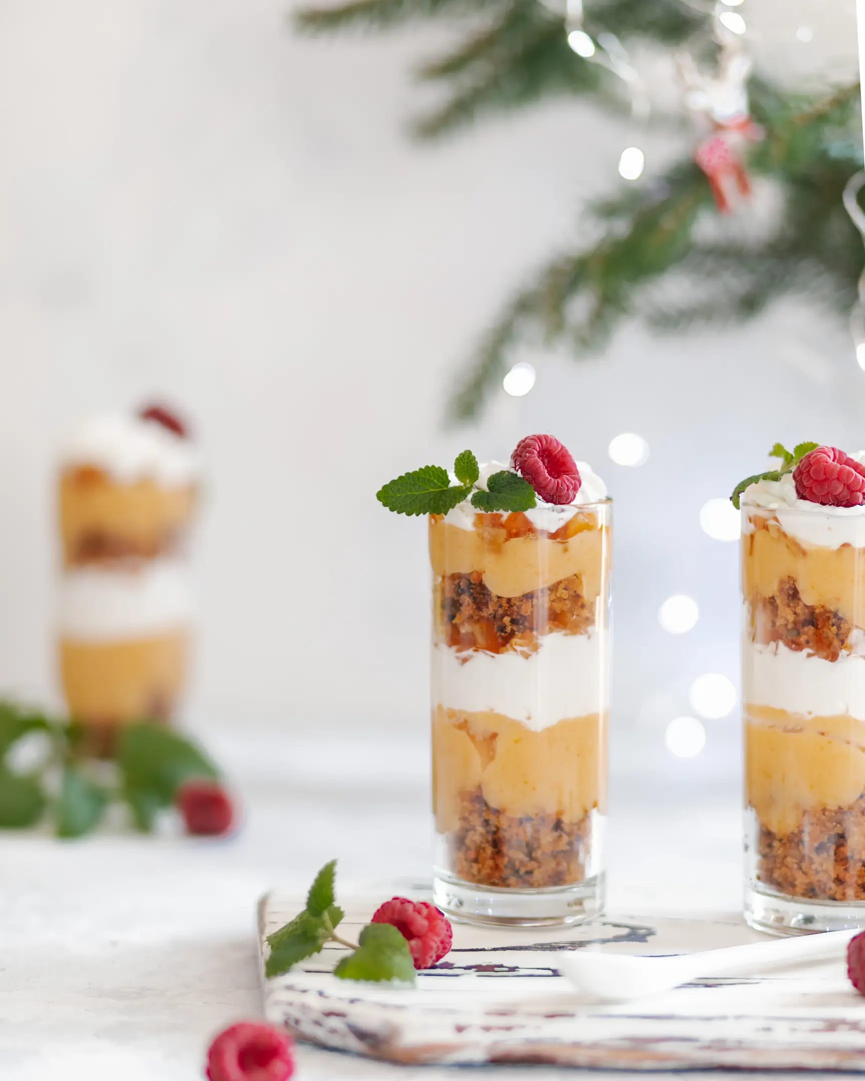 Two tall glasses of festive carrot cake trifles with persimmon-orange cream, Chantilly, fresh raspberries & mint.
