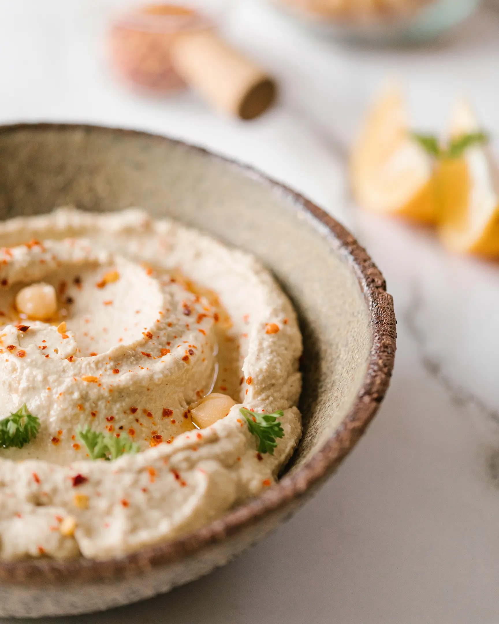 Creamy Middle Eastern hummus dip, garnished with olive oil, pepper flakes, fresh parsley & chickpeas, with lemon wedges.