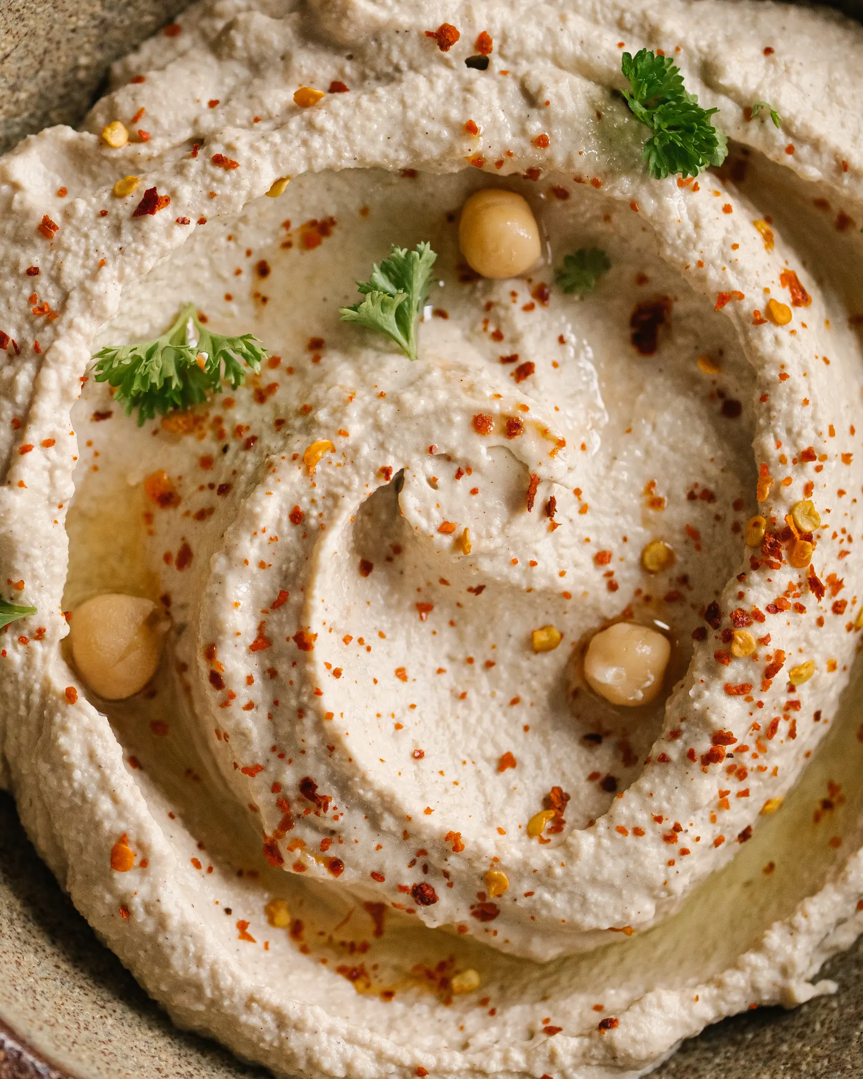 Close-up of creamy Middle Eastern hummus, garnished with chickpeas, olive oil, & pepper flakes.