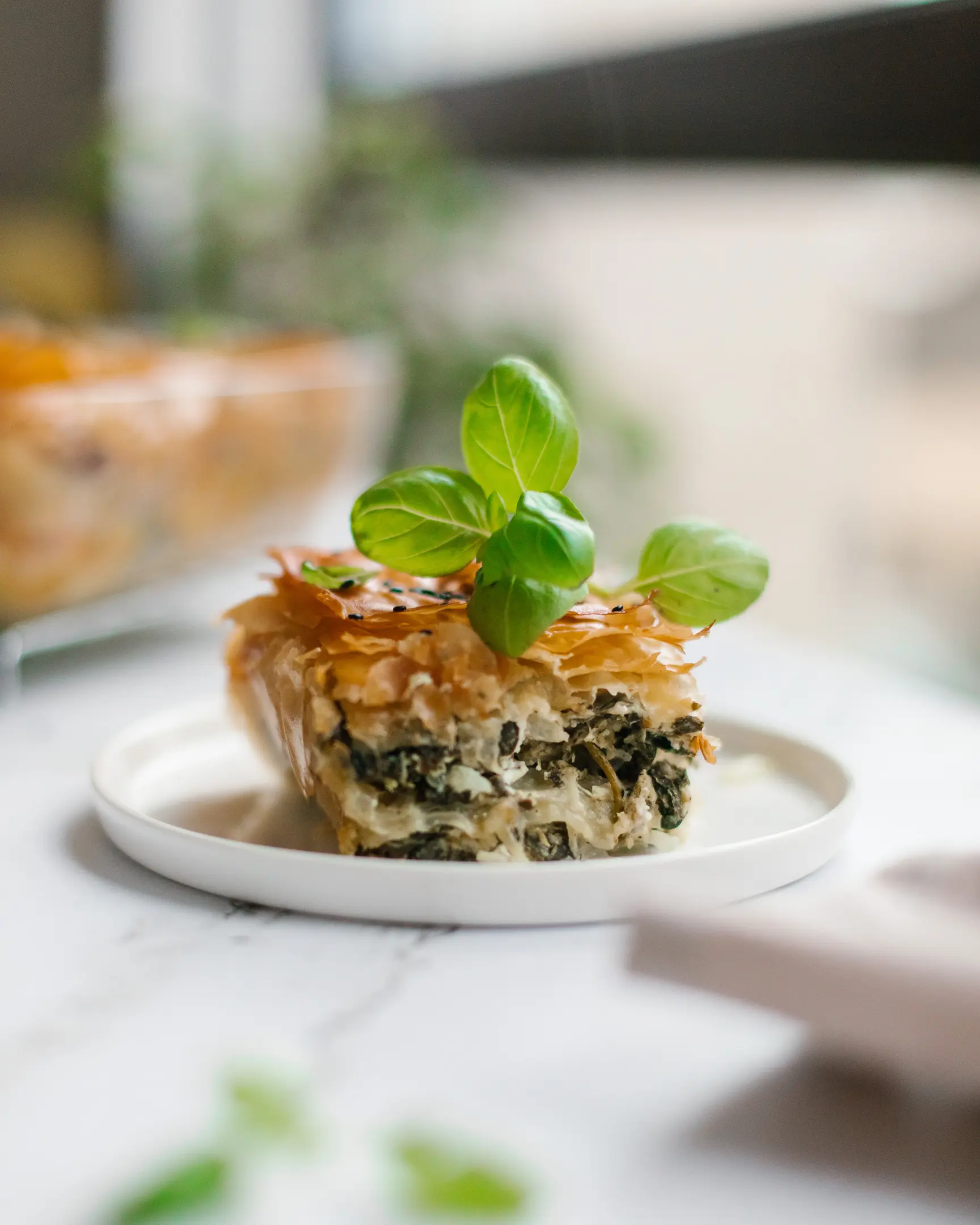 Appetizing slice of Greek spanakopita, showing flaky filo pastry, spinach & feta cheese filling, garnished with basil.