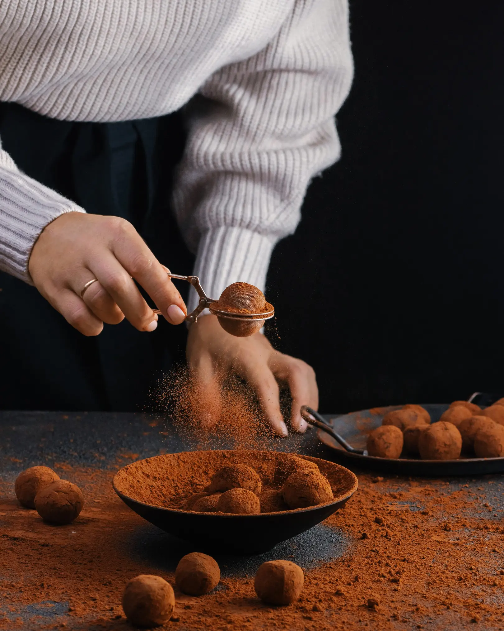 Hands sifting cocoa powder onto chocolate fudge balls, made with sweet condensed milk & espresso for a rich treat.
