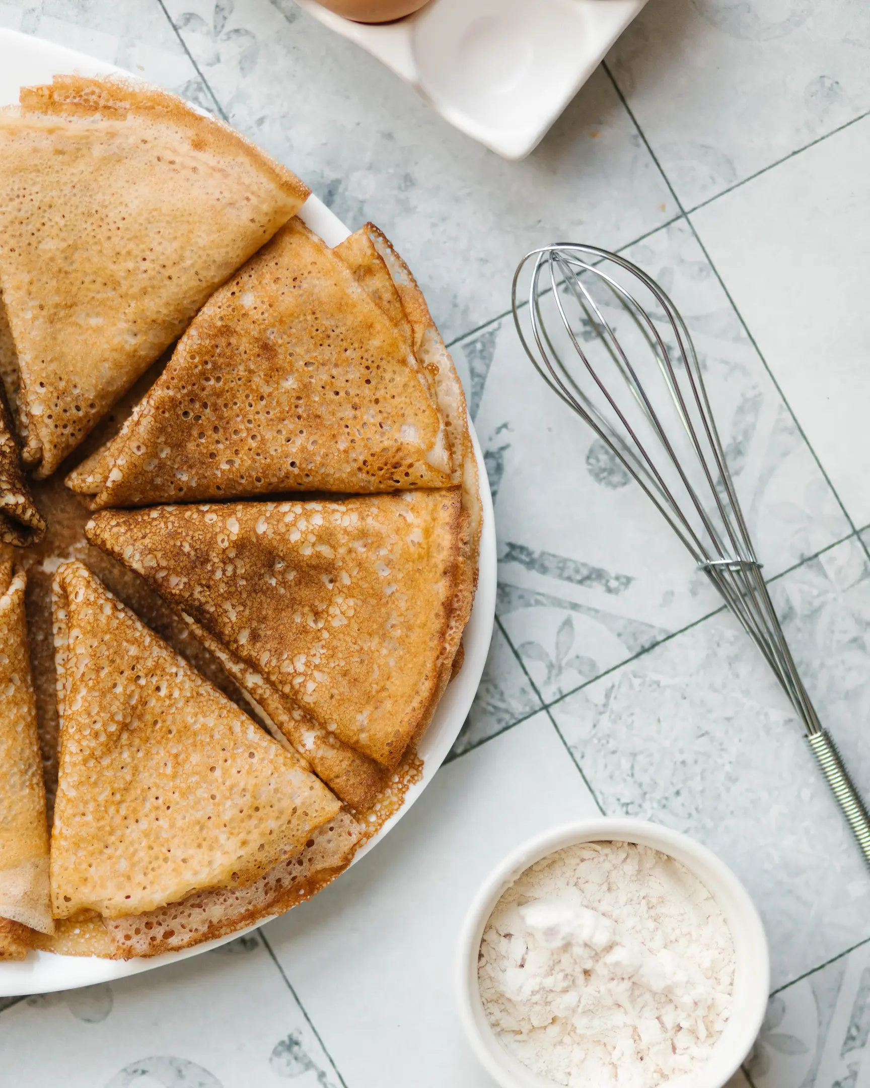 Златни палачинки с хрупкави краища в чиния, с бъркалка, яйца и брашно; за вкусна домашна рецепта.