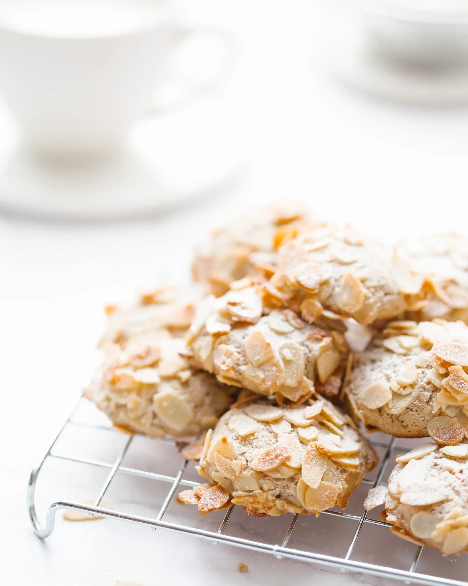 Orange almond cookies with flakes & powdered sugar on a cooling rack.