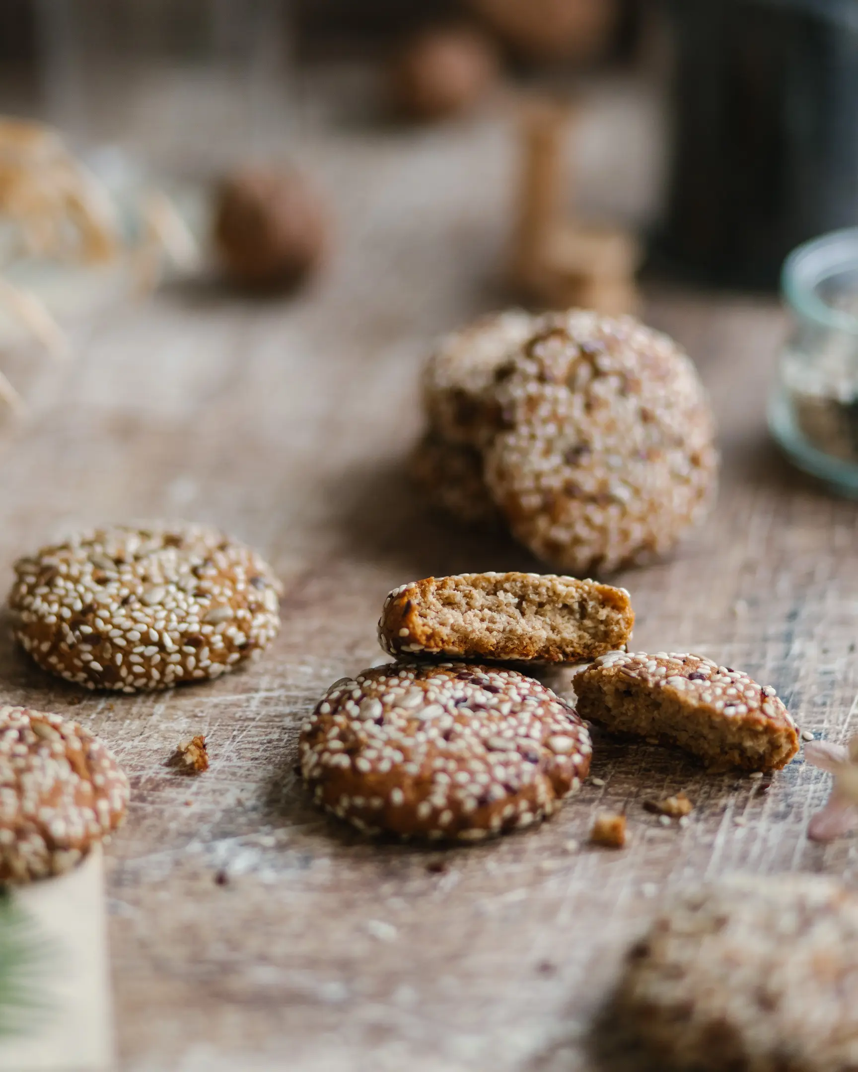 Crispy vegan sesame tahini cookies coated in sesame & mixed seeds, one broken open to show the nutty interior.