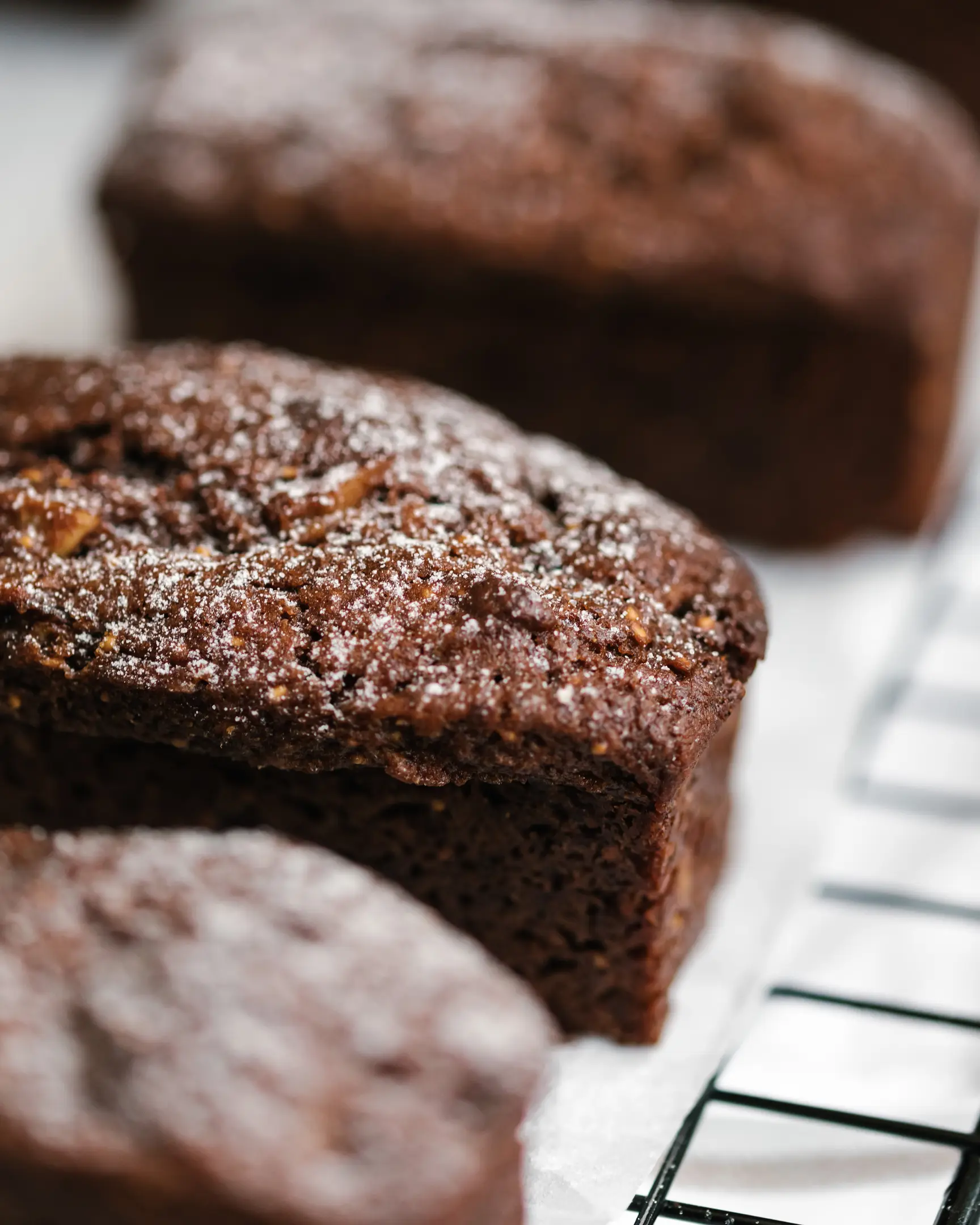 Freshly baked fig and date loaves, featuring Brazil nuts and powdered sugar, cooling on a rack.