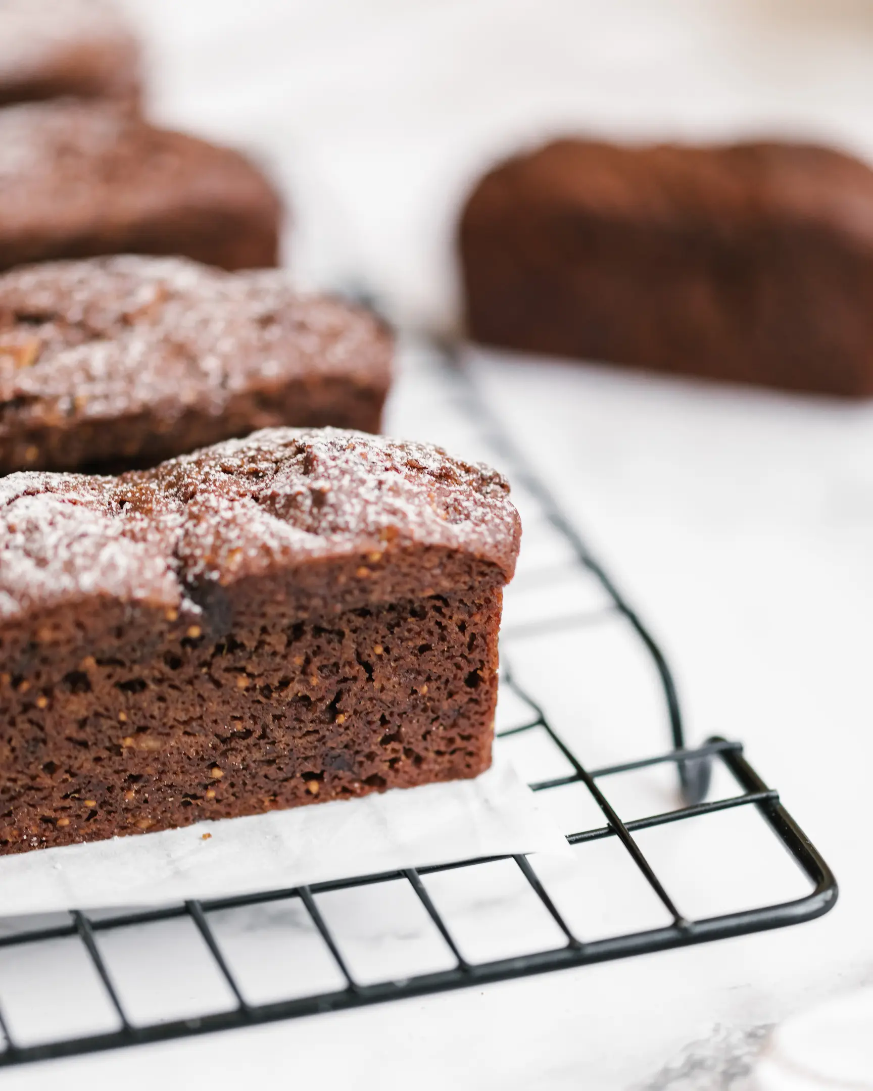 Olya's homemade fig and date cupcakes (mini loaves) with Brazil nuts, dusted with powdered sugar, cooling on a rack.