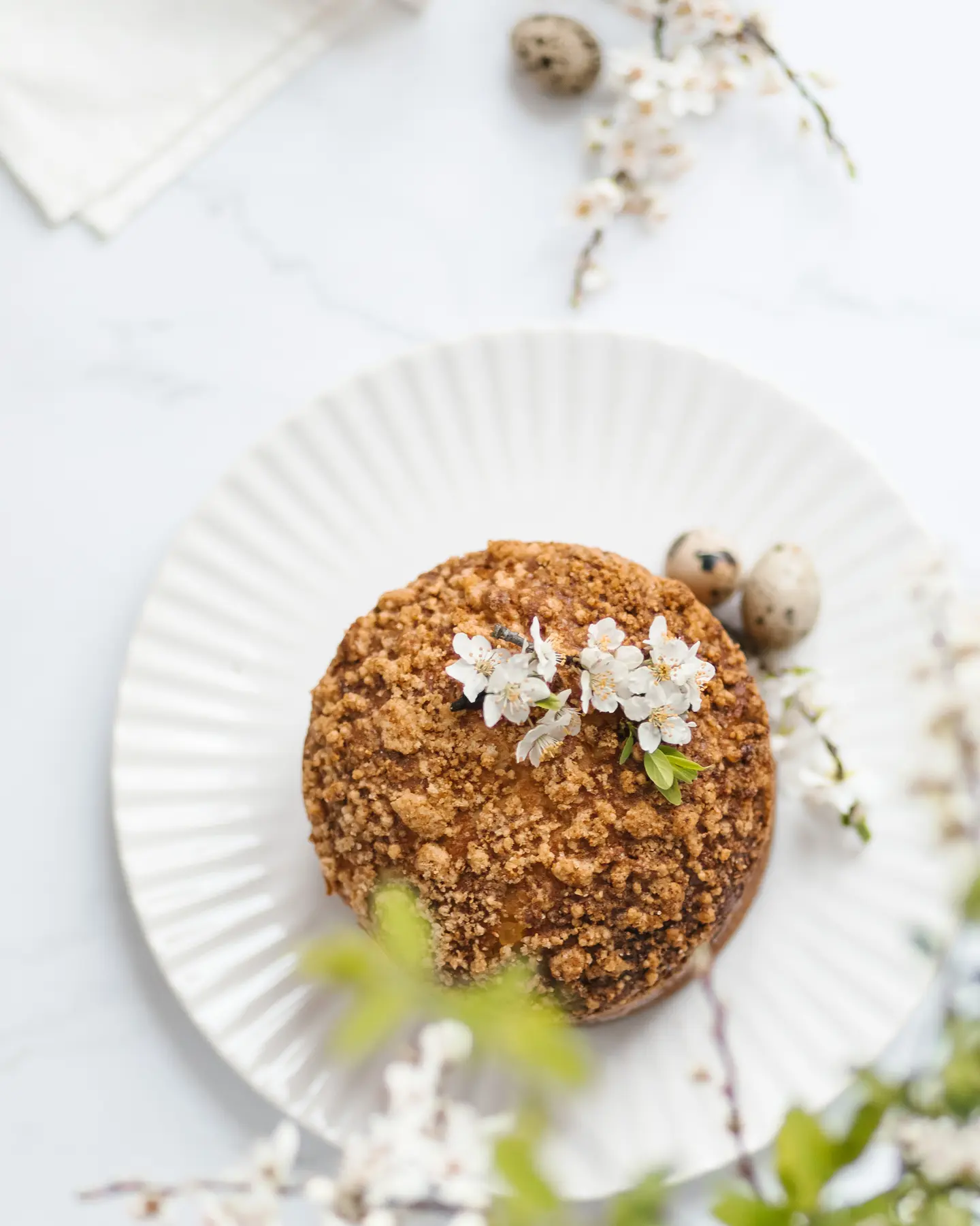 Festive Bulgarian kozunak, a sweet bread with crumble topping, garnished with white blossoms and quail eggs.