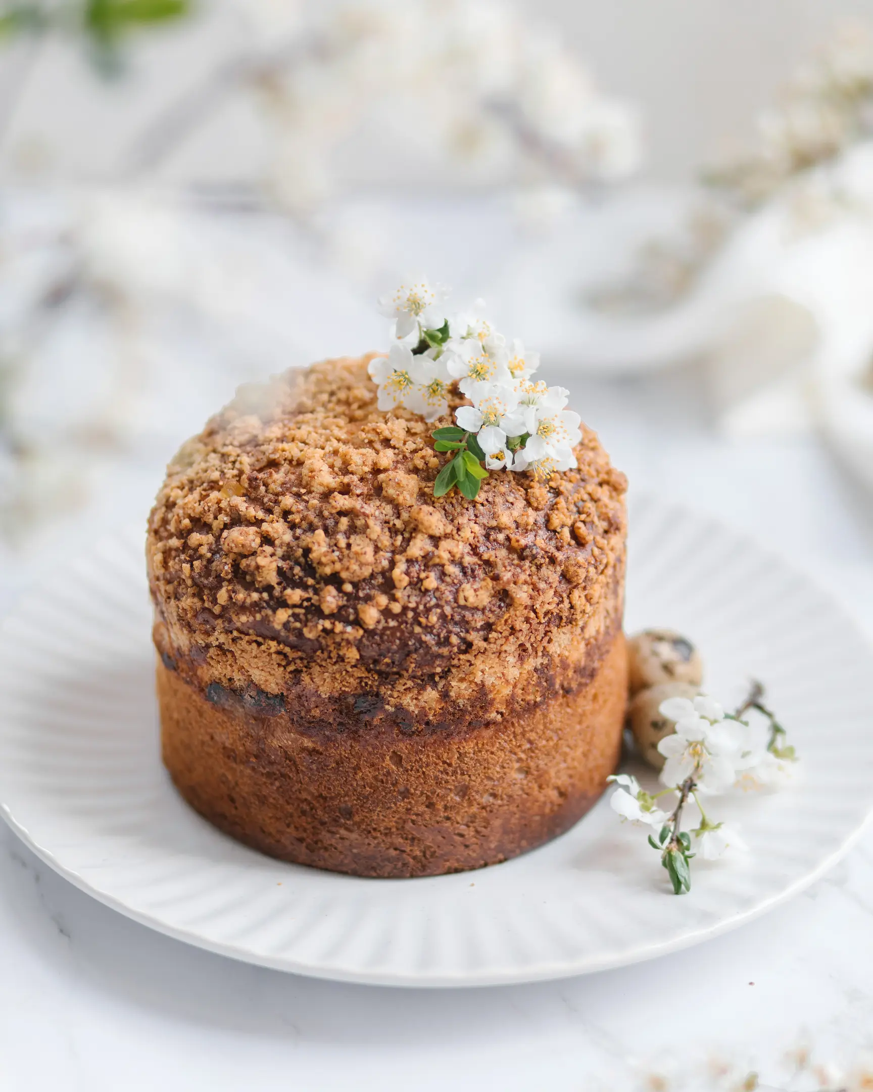 Homemade Bulgarian kozunak with crumb topping, decorated with white blossoms on a white plate.