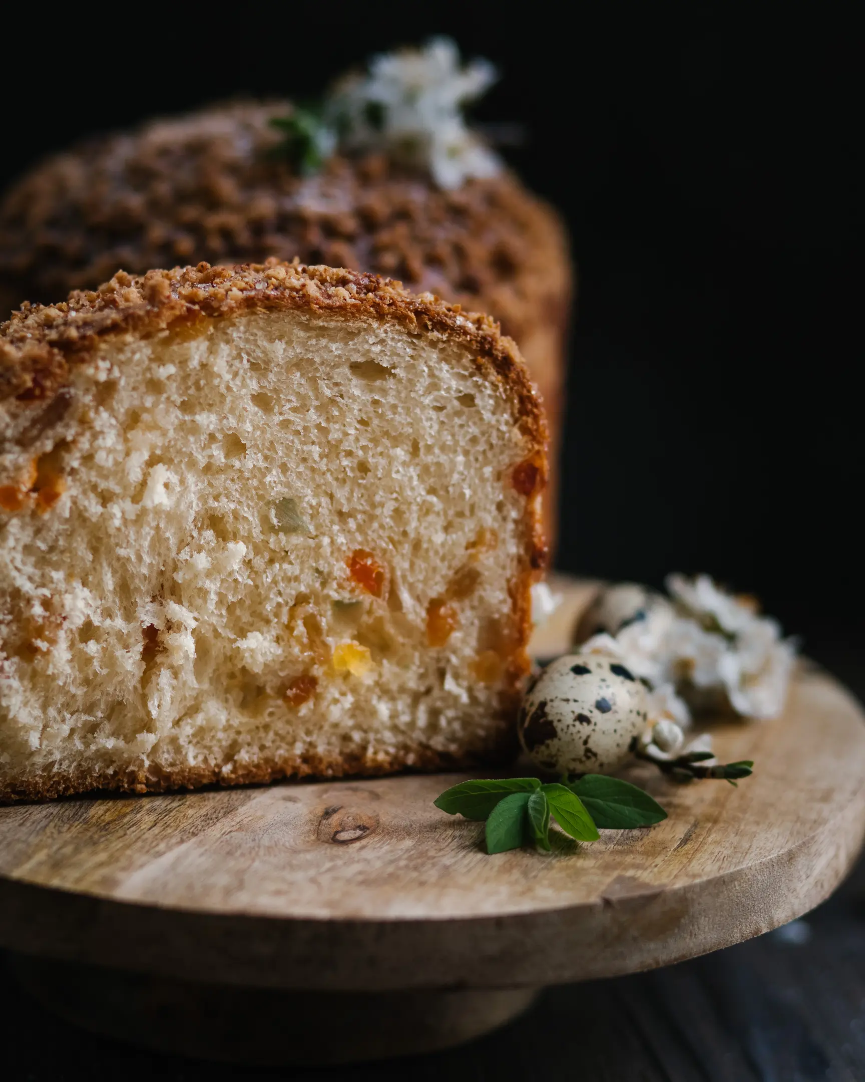 Bulgarian kozunak slice with candied fruits & crumble, on a wooden board, decorated with quail eggs.