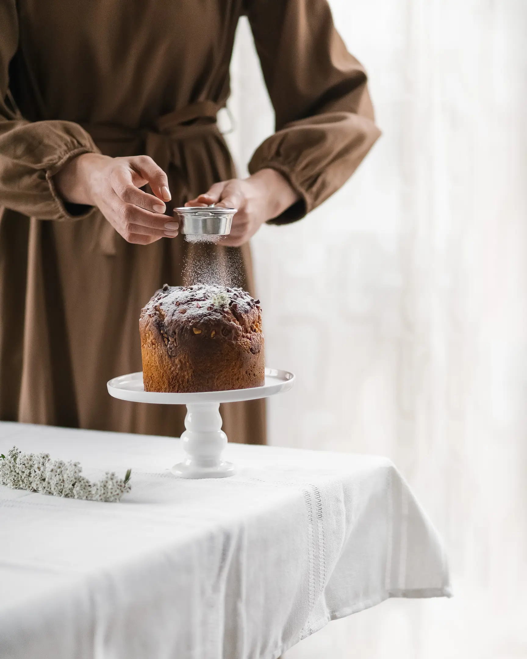Woman sprinkling sugar on Grandmother's Manya Easter cake, baked with chopped nuts.