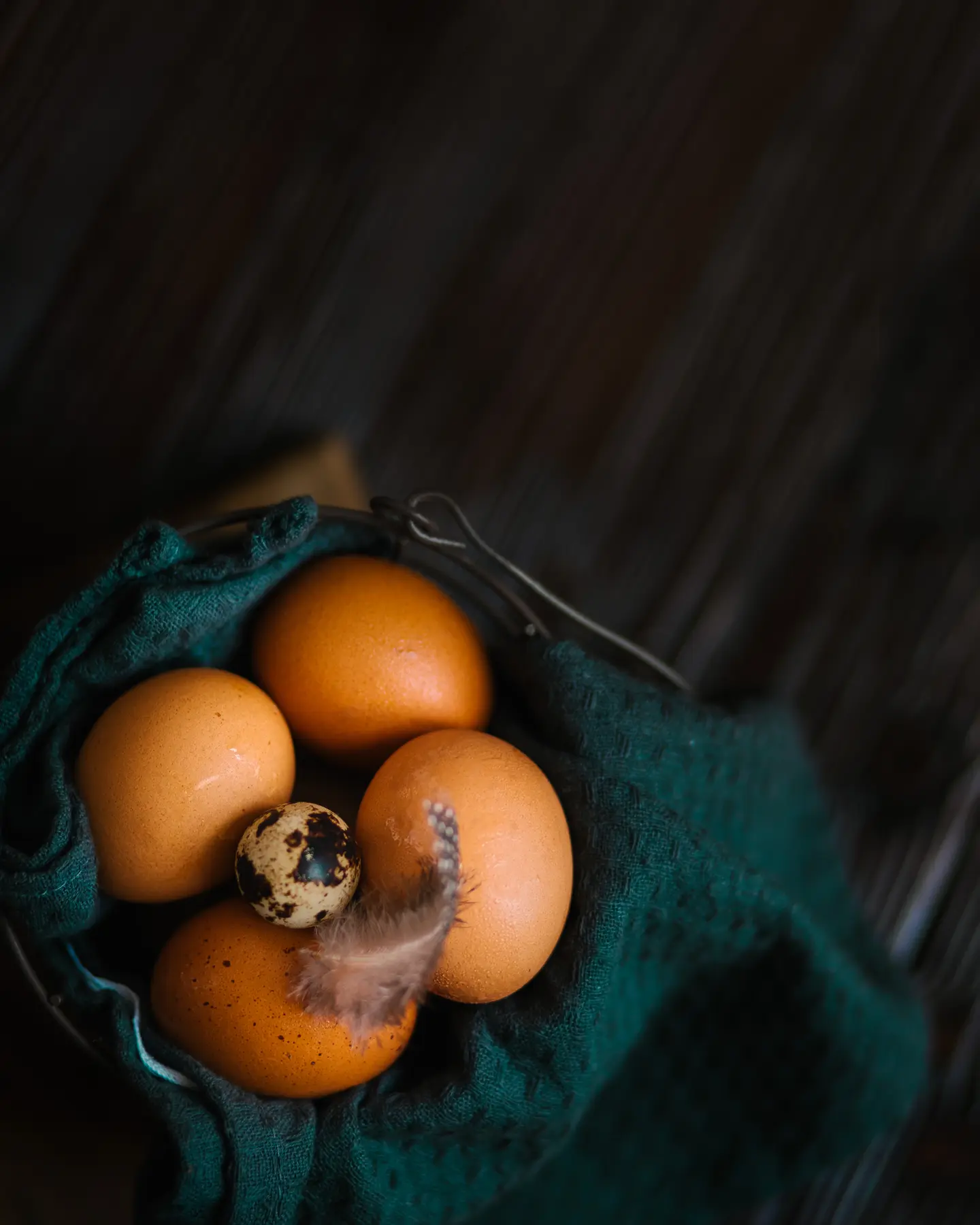 Brown and quail eggs with a feather in a teal basket, key ingredients for homemade Easter bread.
