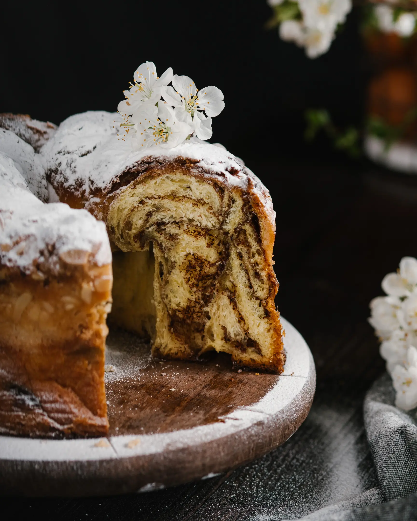 Fresh Easter Bread, dusted with powdered sugar & white blossoms, reveals its cinnamon sugar swirl filling.