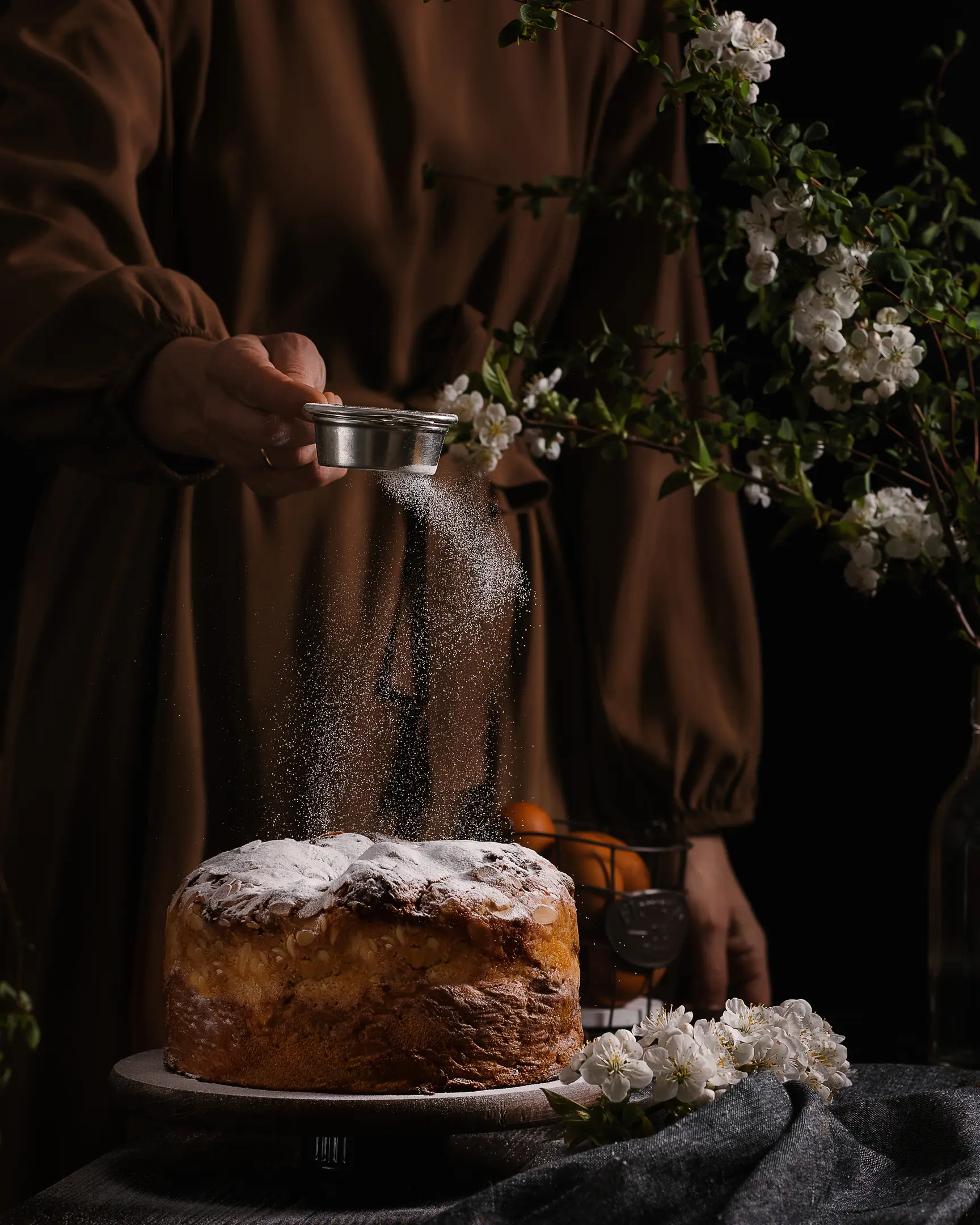 Woman sprinkling sugar on Grandmother's Manya Easter cake, baked with chopped nuts.