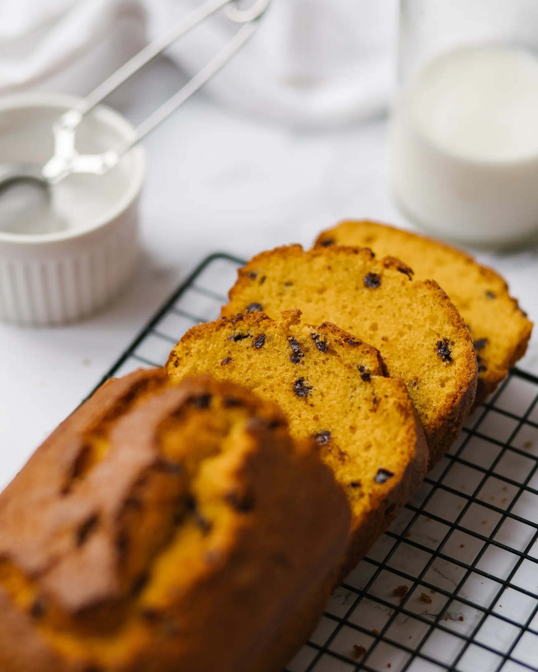 Bright yellow easy carrot cake with chocolate drops, sliced and cooling on a pastry rack.