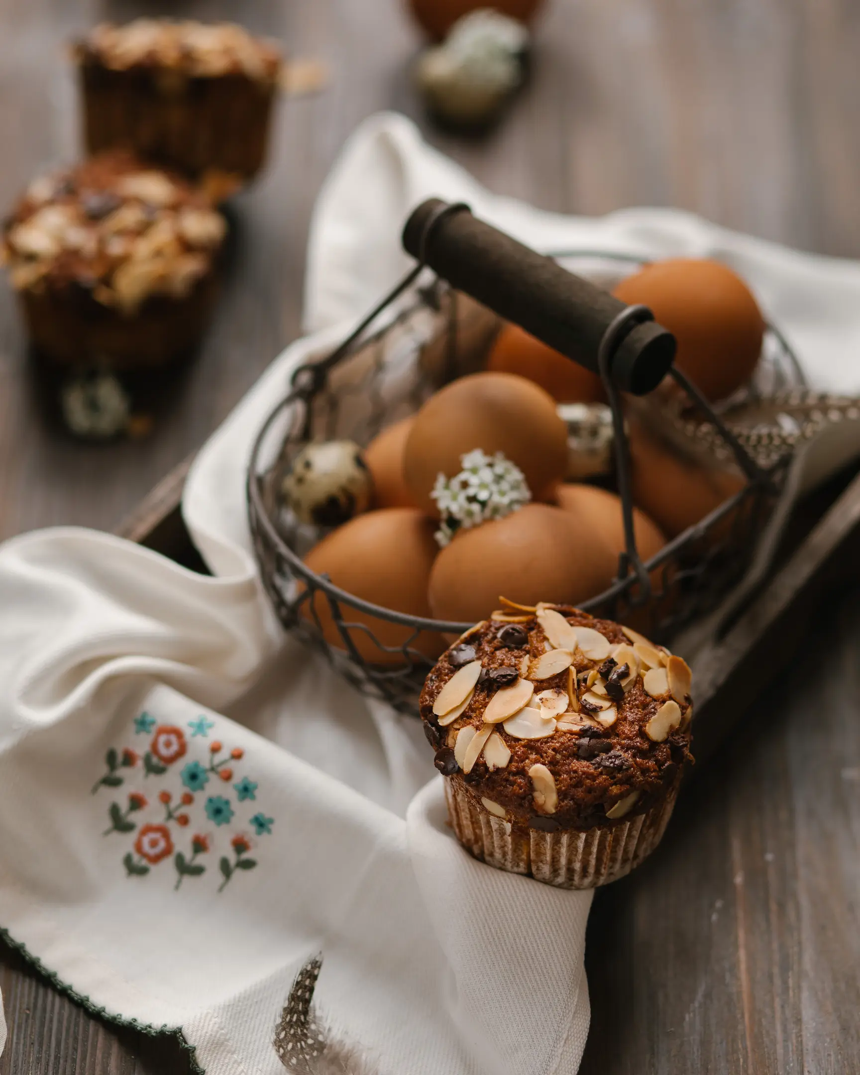 Healthy Banana Carrot Muffin topped with almond petals & chocolate, with baking eggs in a basket.