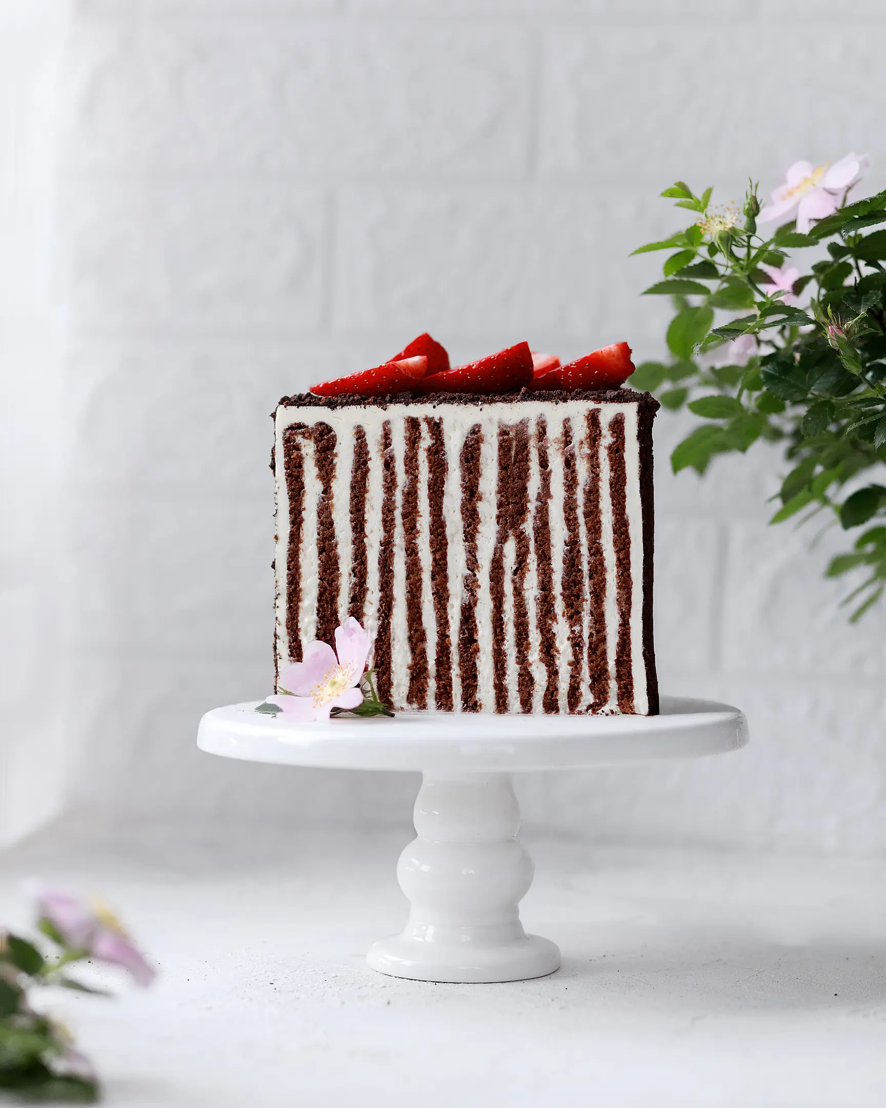 Tall honey cocoa cake slice with vertical cream cheese layers, topped with fresh strawberries. Recipe.