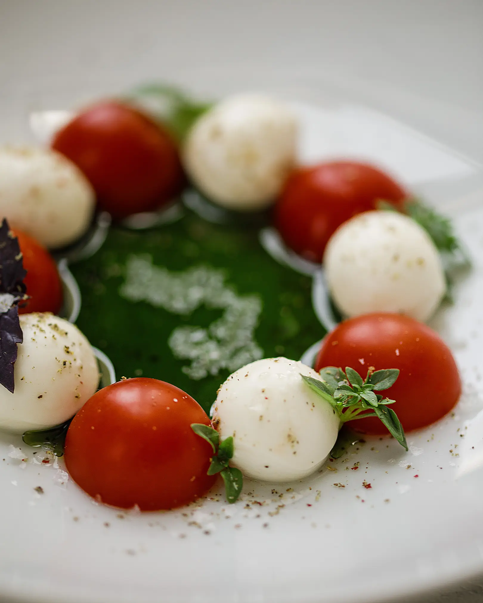Caprese salad with cherry tomatoes, mozzarella cheese, and green oil, garnished with basil and seasoning.