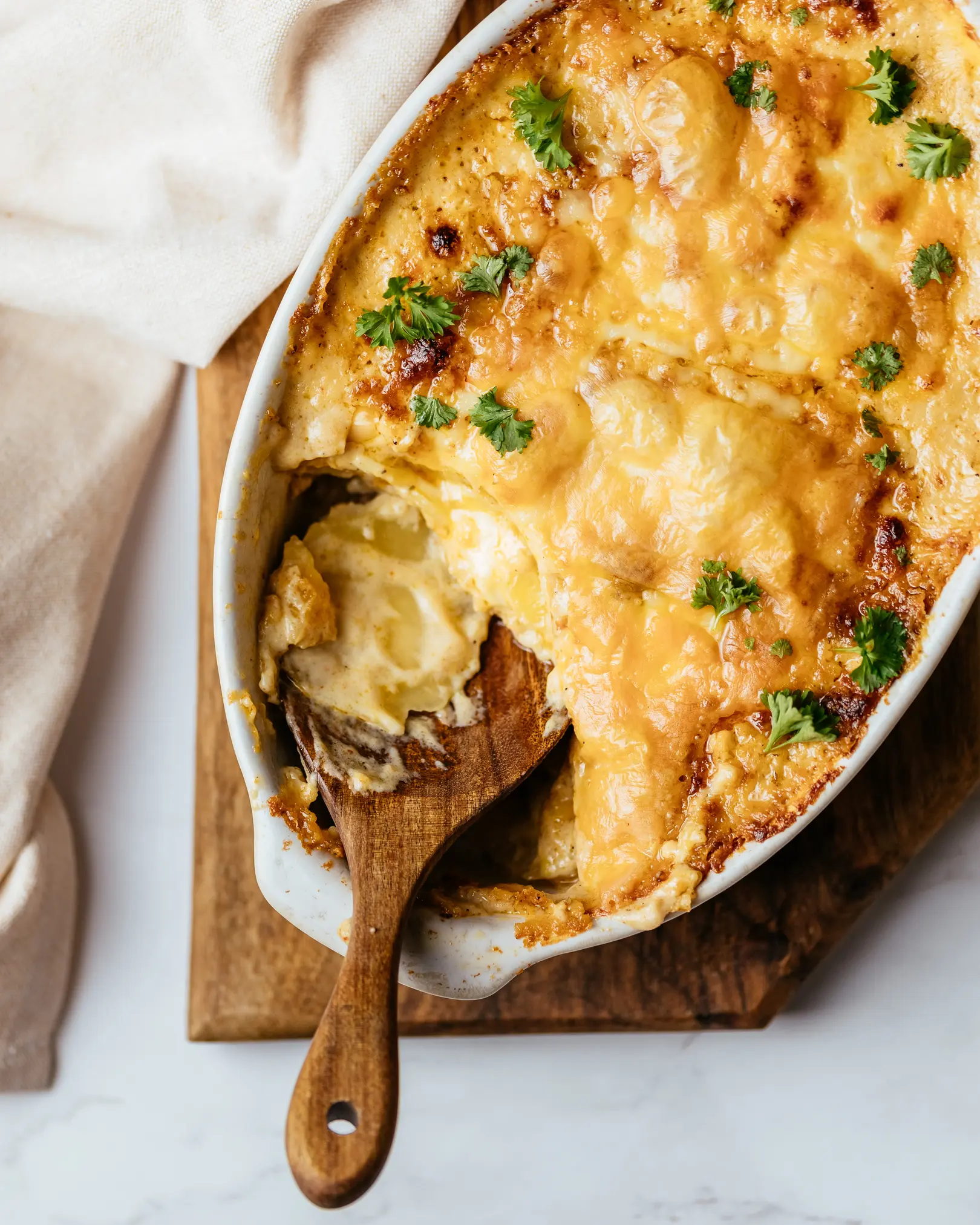 Golden-brown vegetarian potato casserole with creamy sauce, melted cheese, and parsley, ready to serve with a wooden spoon.