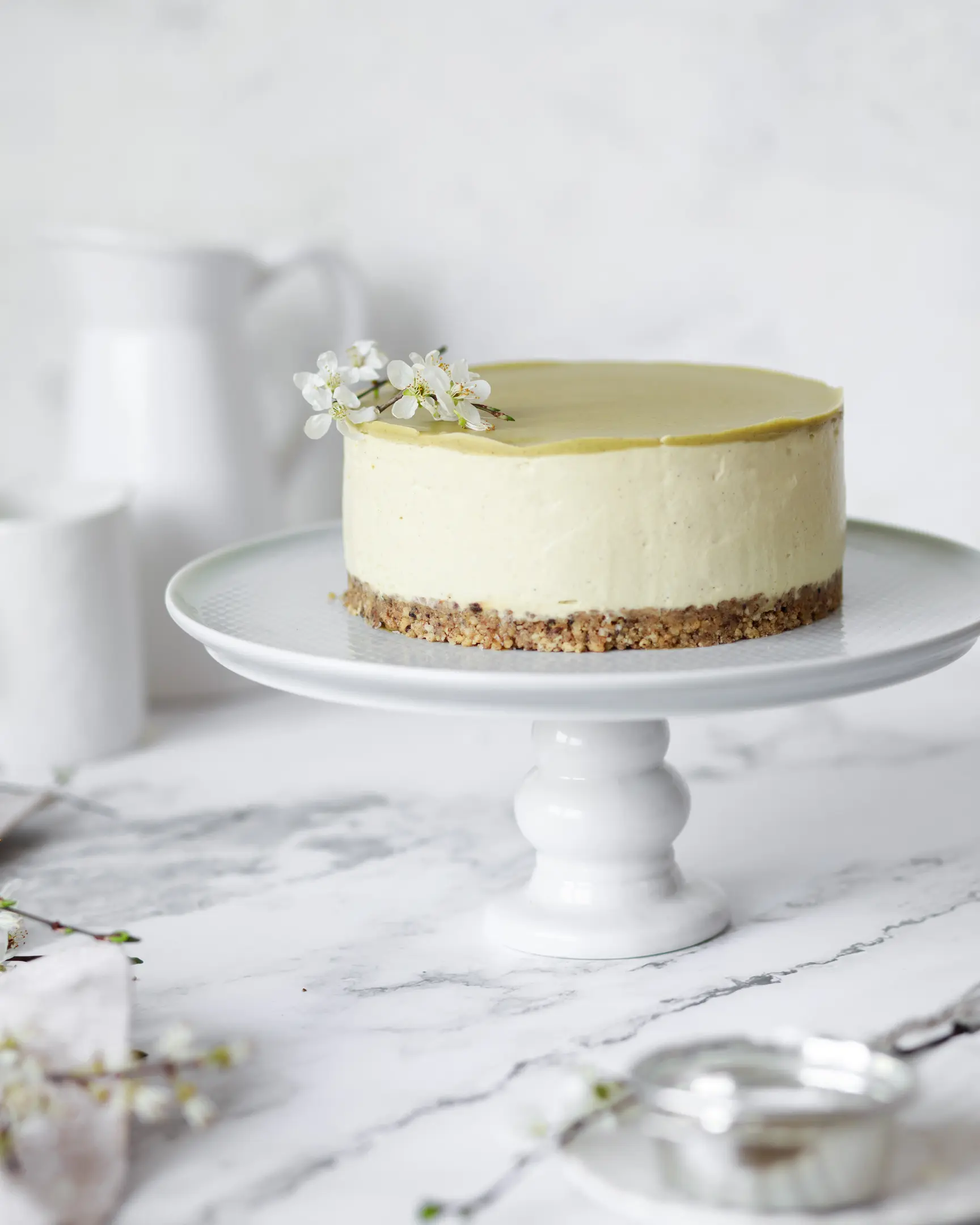 No-bake pistachio cheesecake with cookie base & white chocolate, made with Philadelphia cream cheese, on a stand.