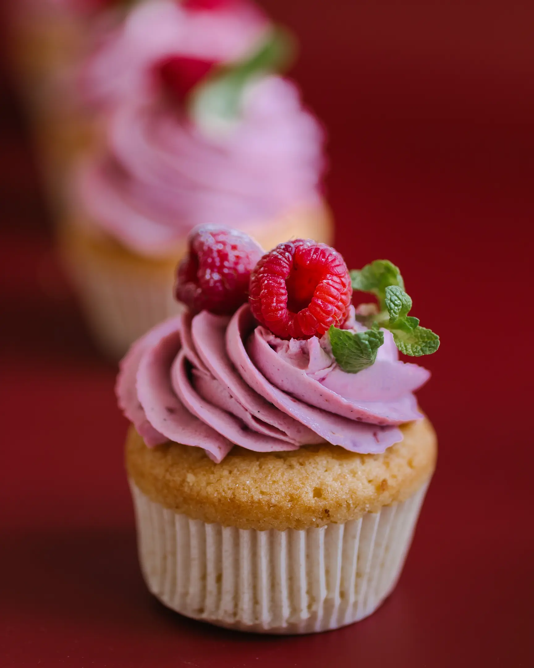 Moist vanilla cupcake with pink raspberry mascarpone frosting, topped with fresh raspberries & mint.