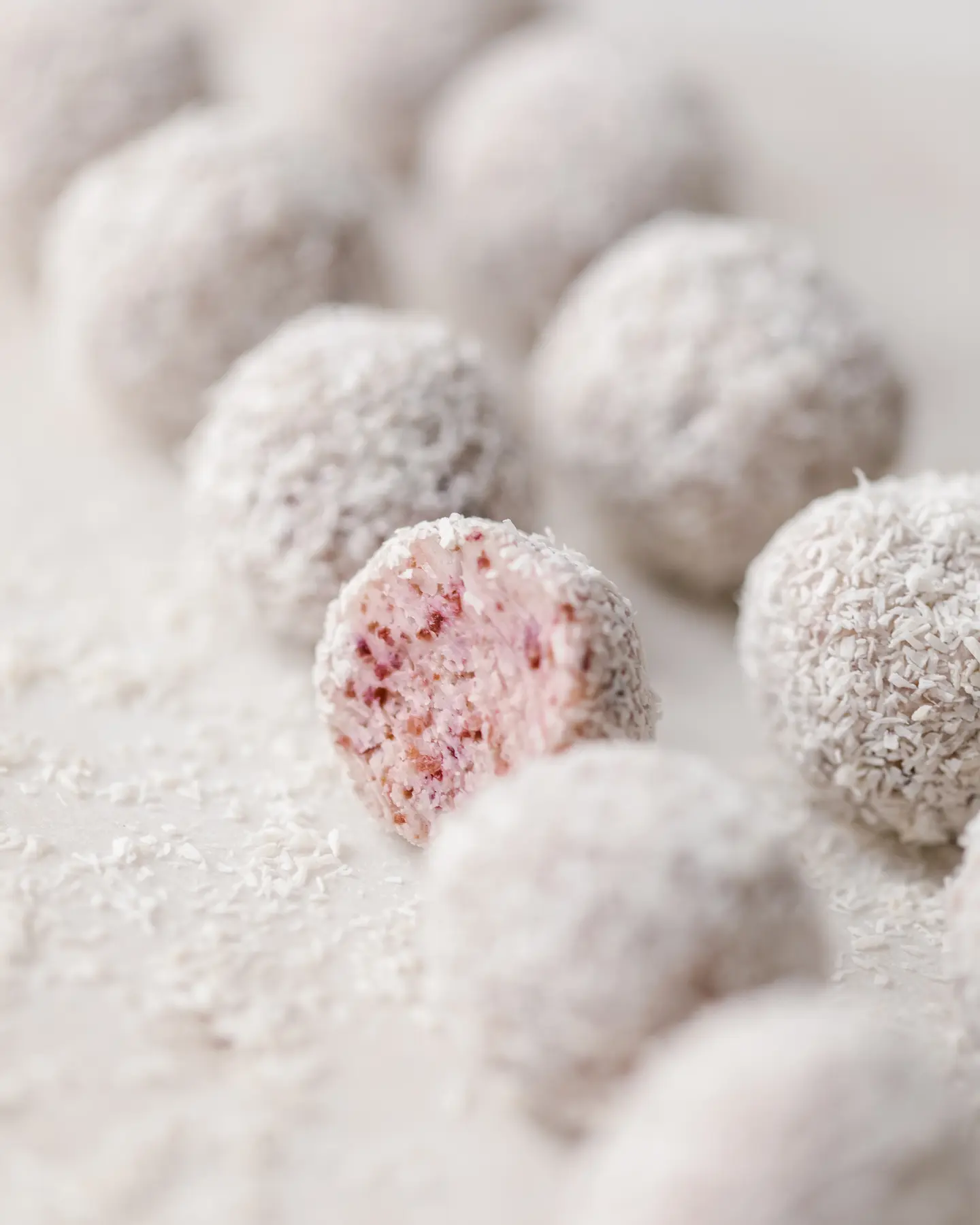 Homemade Cranberry truffles coated in coconut flakes, one showing pink interior of dried cranberries & white chocolate.