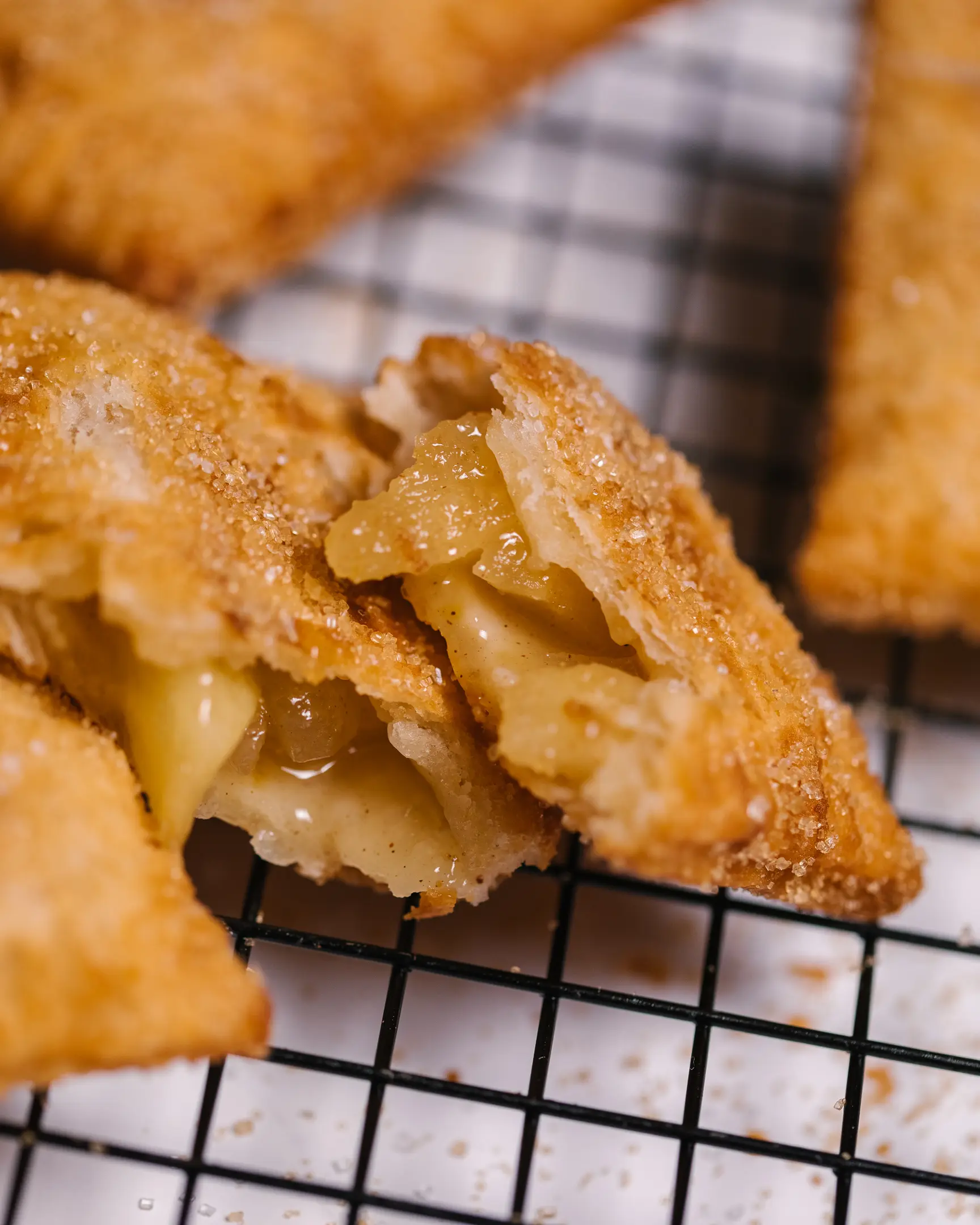 Златистокафяв ябълков пай, разчупен да покаже сочен пълнеж, поръсен със захар и канела, върху решетка за охлаждане.