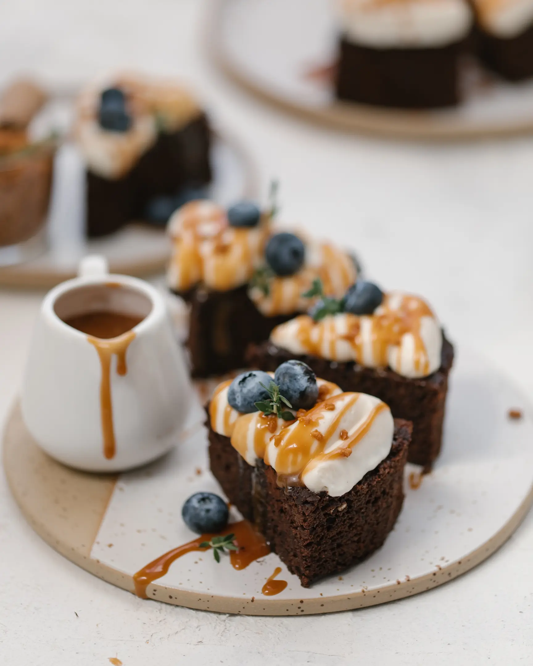 Chocolate Banana Cake portions with mascarpone cream, caramel drizzle, fresh blueberries, and a caramel pitcher.