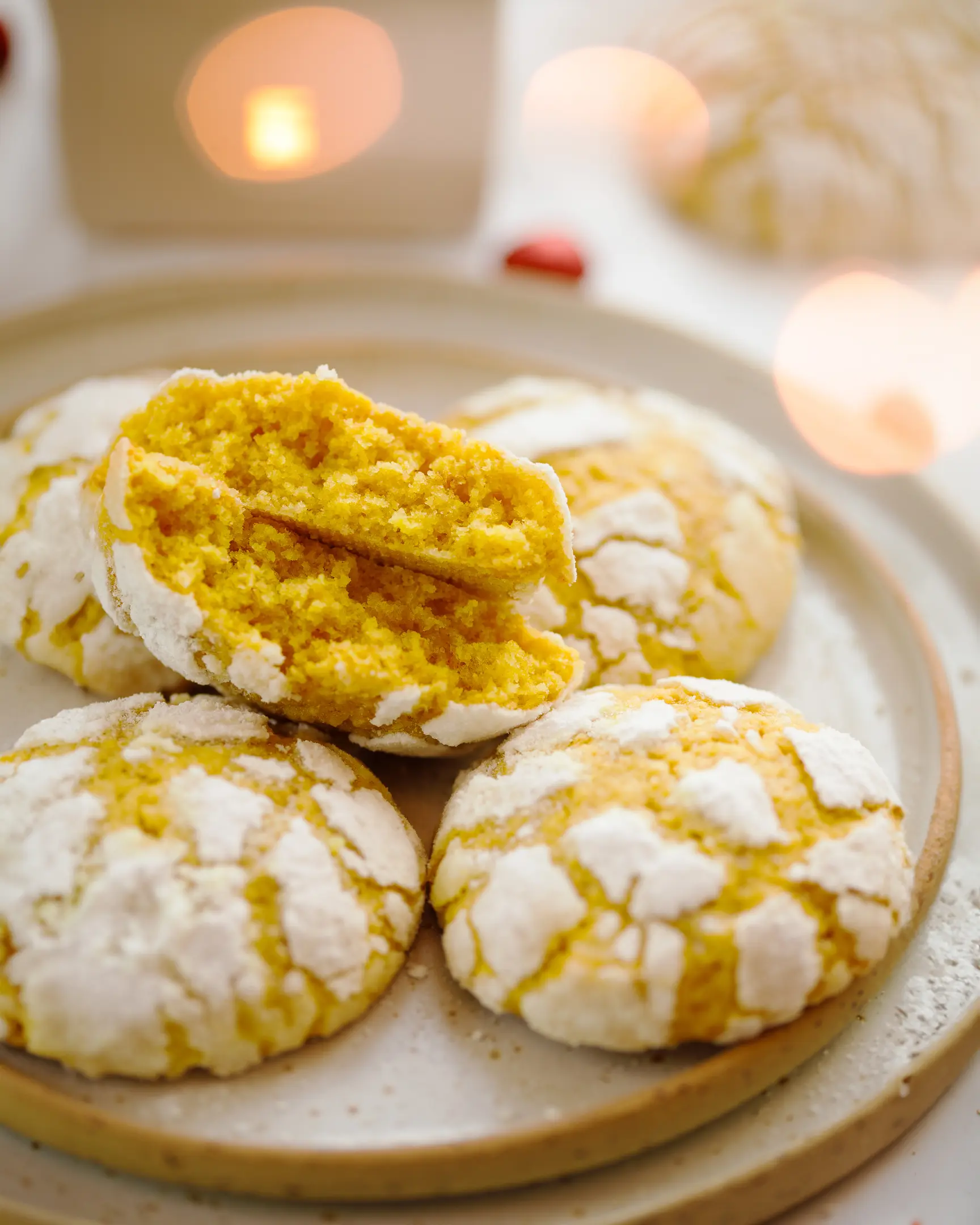 Orange crinkle cookies with perfect powdered sugar cracks on a plate, one broken to reveal the soft, citrusy interior from the recipe.