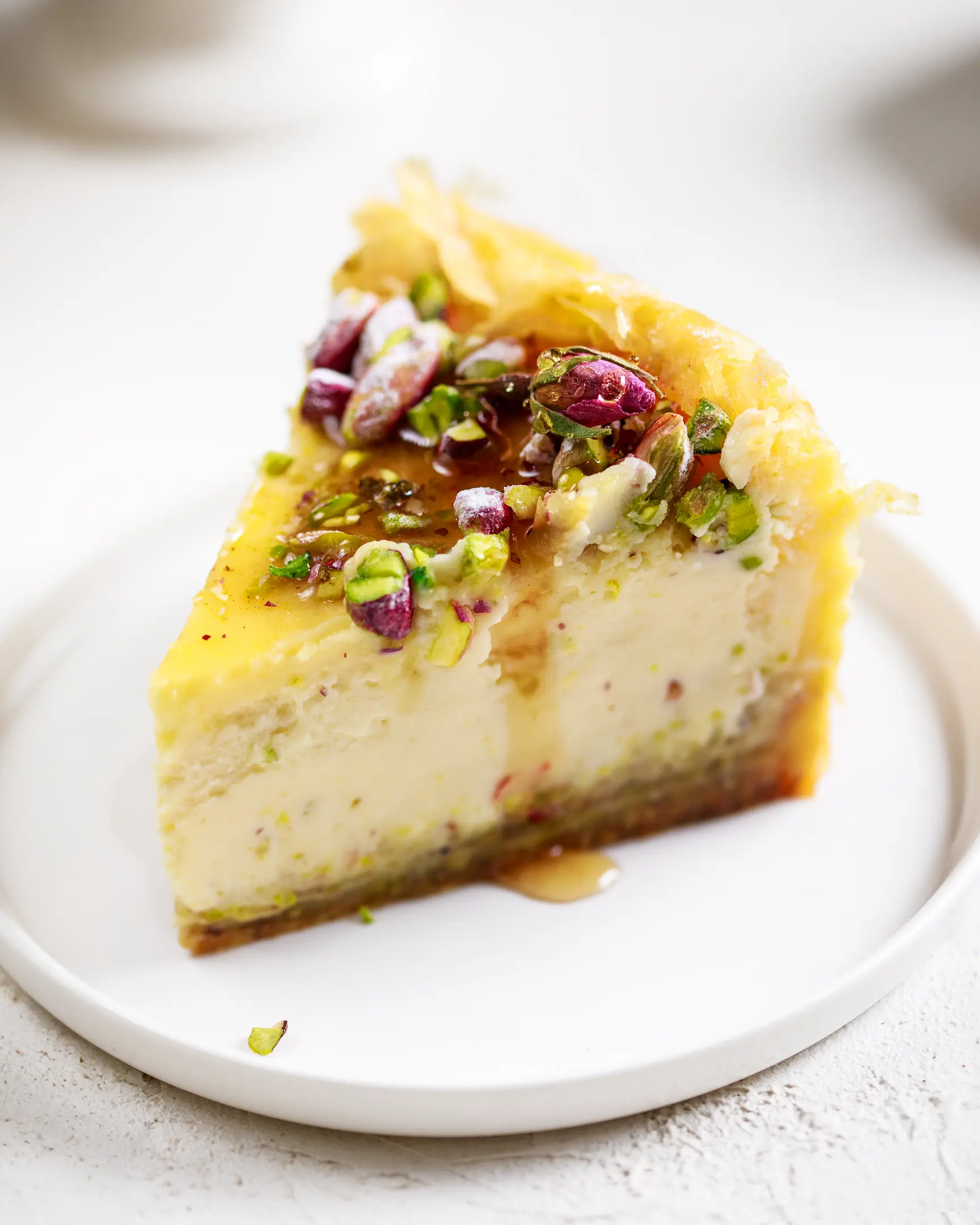 Slice of Baklava Cheesecake with crinkly phyllo crust, creamy filling, vibrant pistachio topping, and honey syrup drizzle.