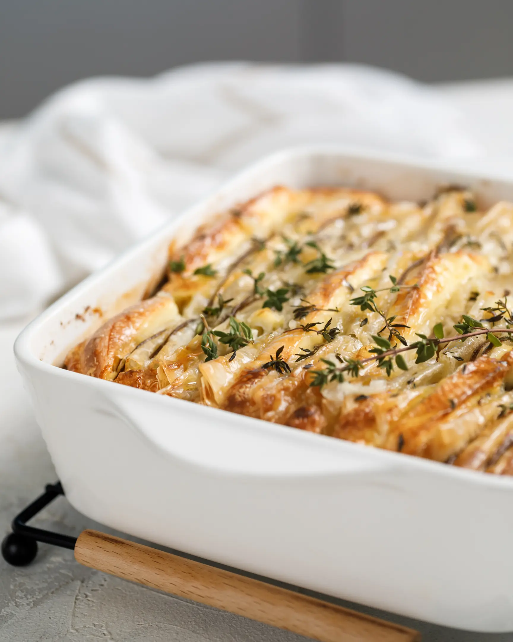 Златист тарт от фило със сирене Бри и резени круша, поръсен със свежа мащерка, в бяла чиния.