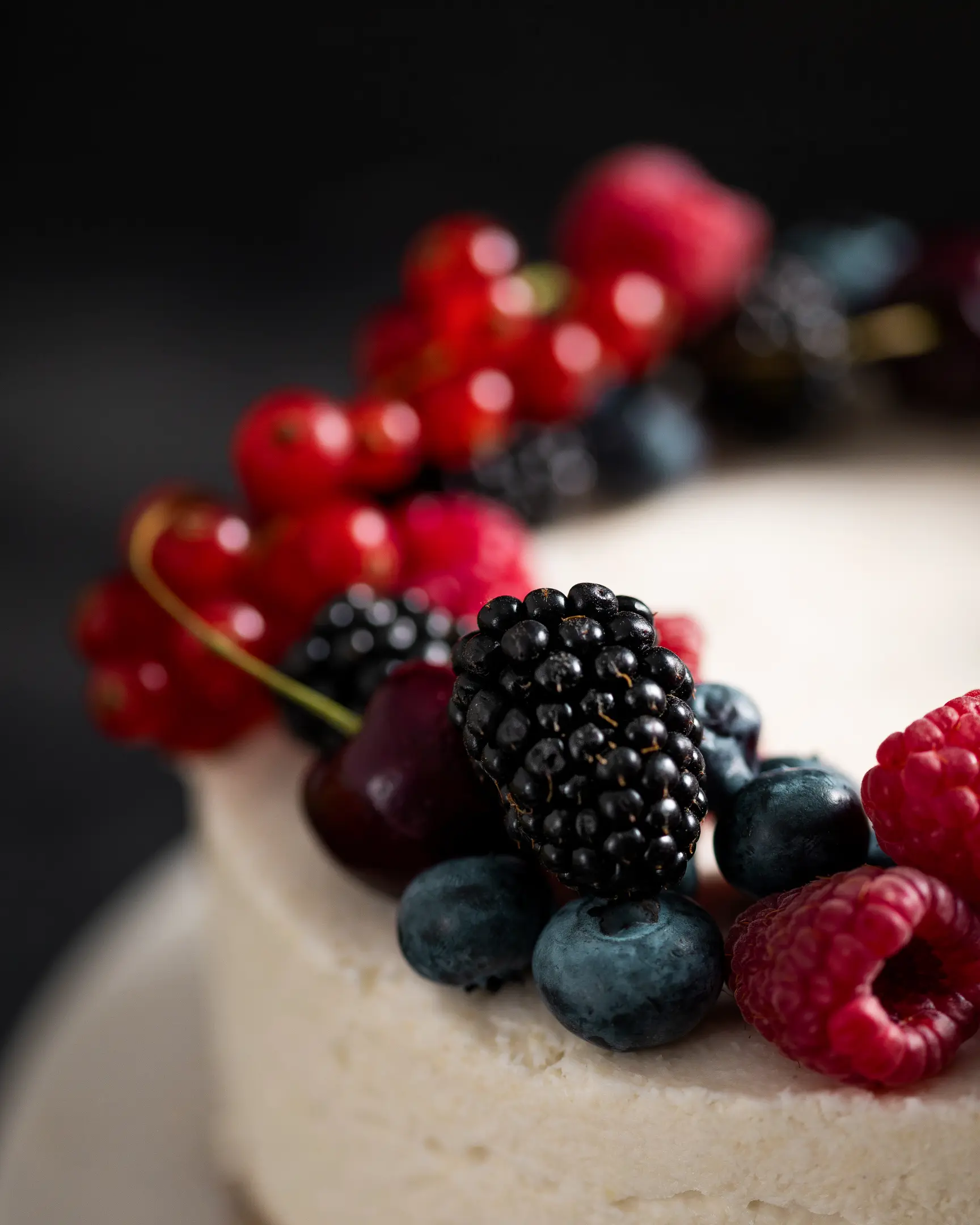 Creamy coconut raw cake adorned with fresh, vibrant berries including blackberries, raspberries, blueberries, and red currants.