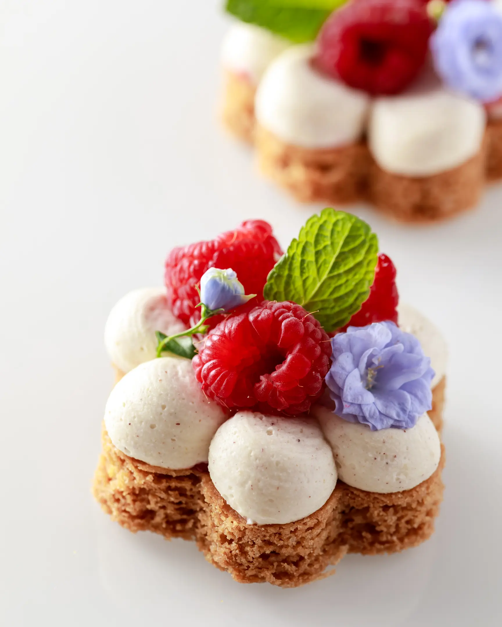 Flower-shaped Sablé Bretons with nut ganache, fresh raspberries, mint, and delicate edible flowers, perfect for dessert.