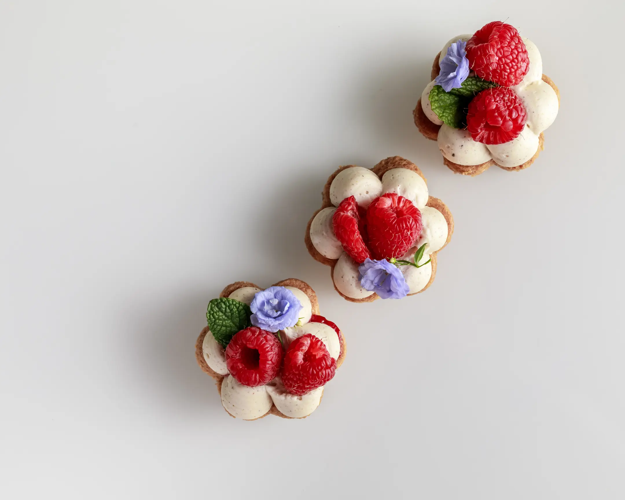 Delicious flower-shaped Sablé Bretons with nut-flavored ganache, raspberry coulis, fresh raspberries, and edible flowers.
