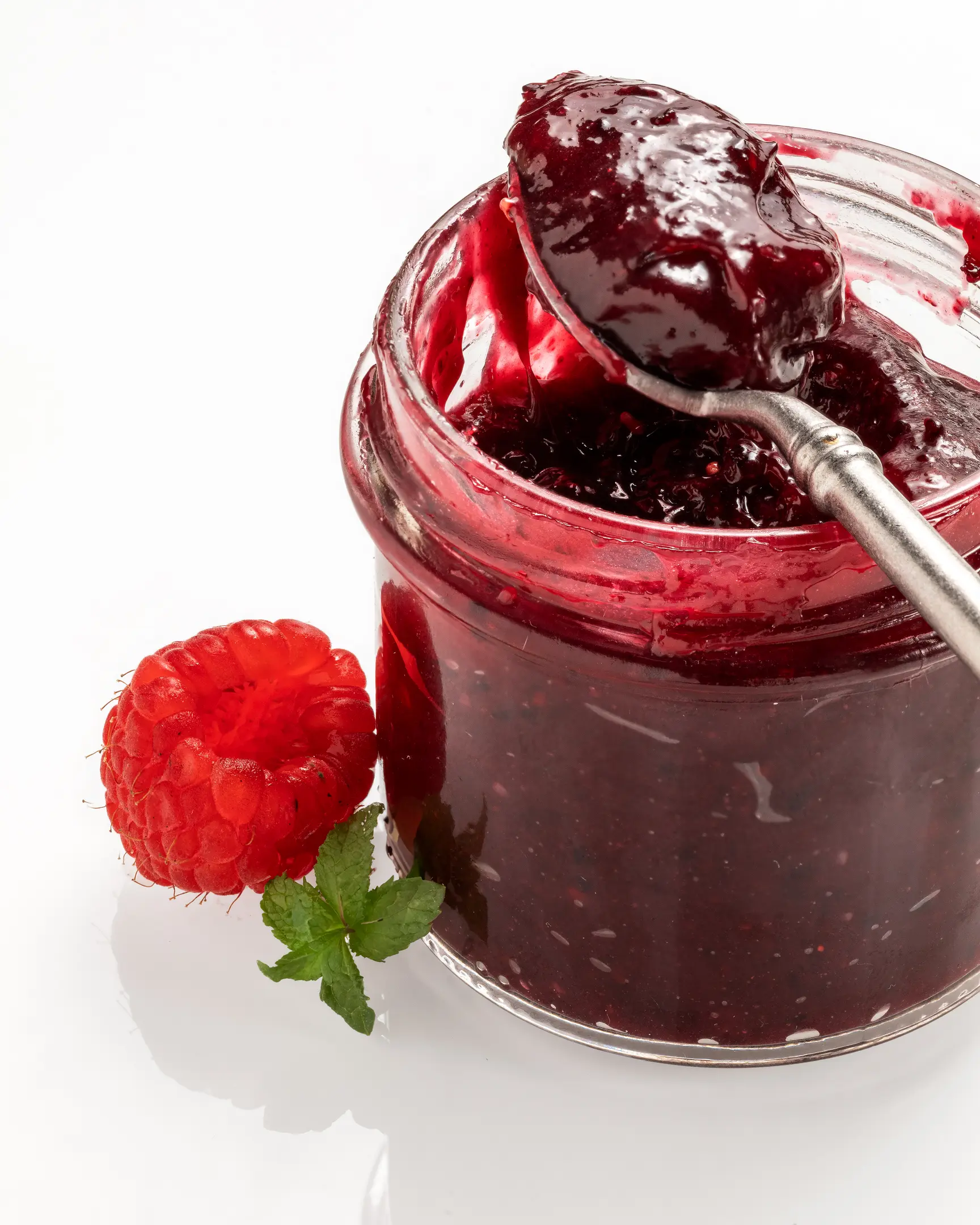 Homemade berries caramel in a jar with a spoon, fresh raspberry & mint. Great for cakes & toast.