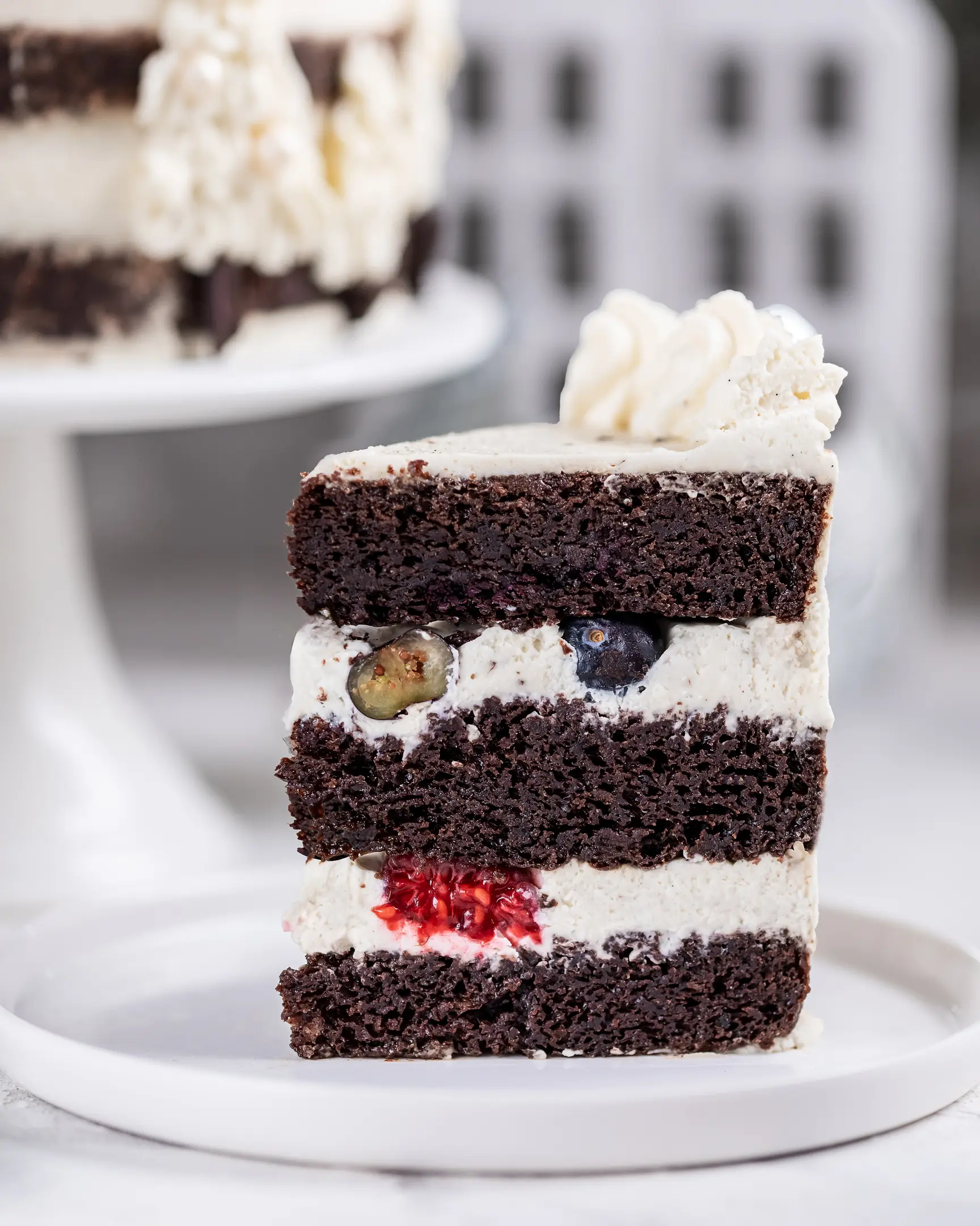 Slice of rich chocolate pumpkin cake with mascarpone cream, blueberries, & raspberries. A moist & indulgent dessert.