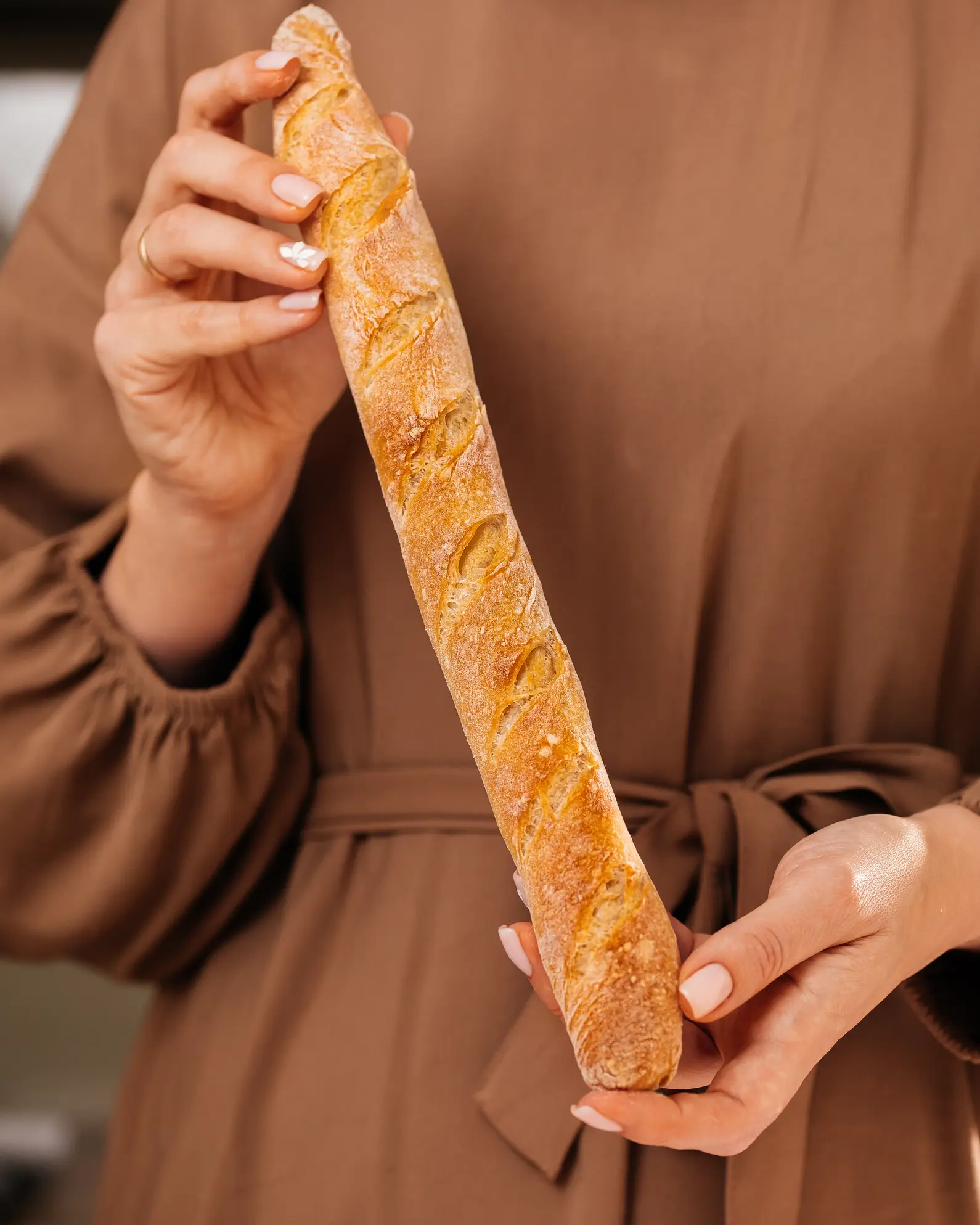 Hands hold a golden, crispy baguette. Made from the recipe's dough, using yeast or sourdough, yielding 270g per baguette.